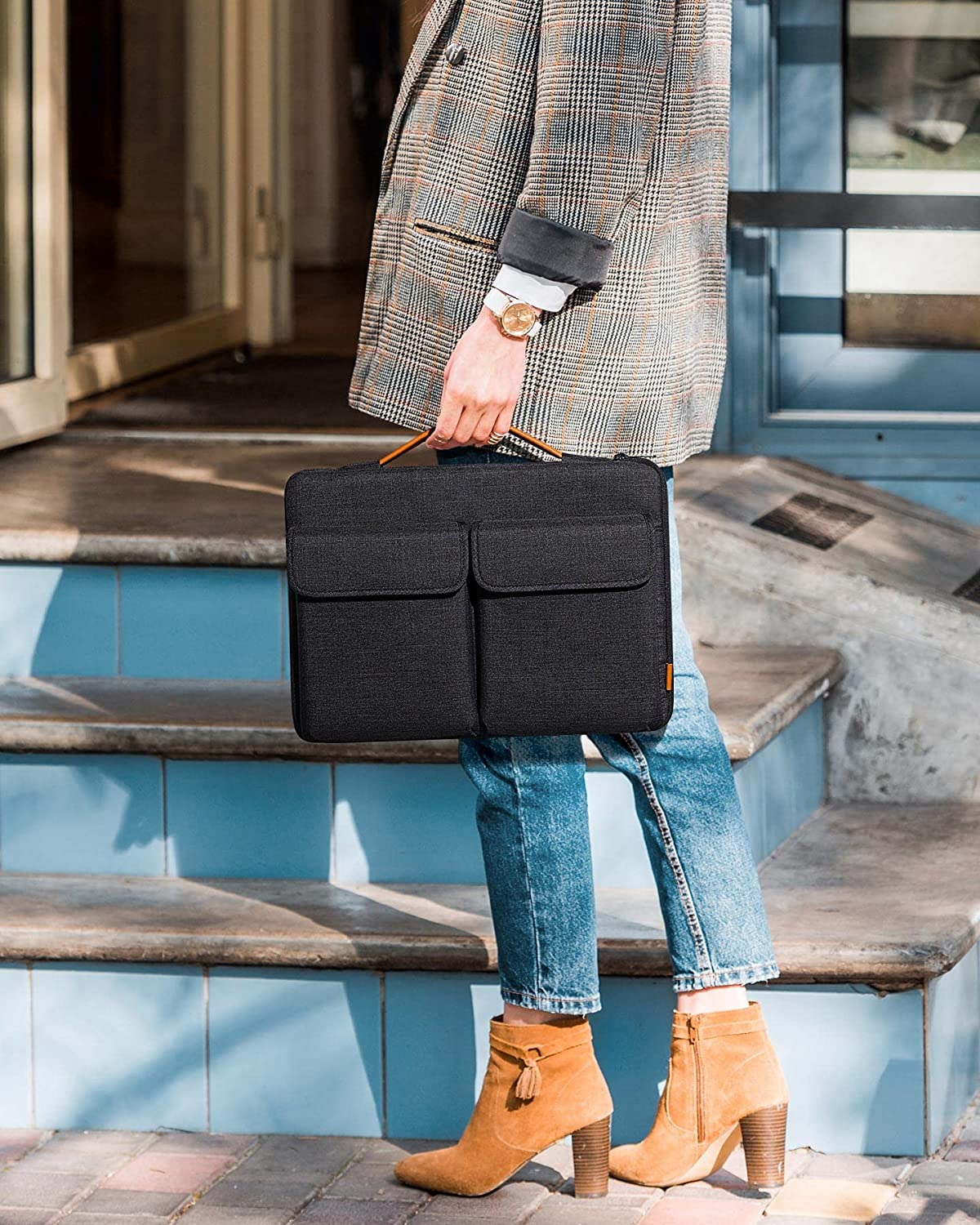 Eine Person hält eine schwarze Laptoptasche mit zwei Vordertaschen. Sie stehen auf blauen Stufen. Die Tasche ist strukturiert.