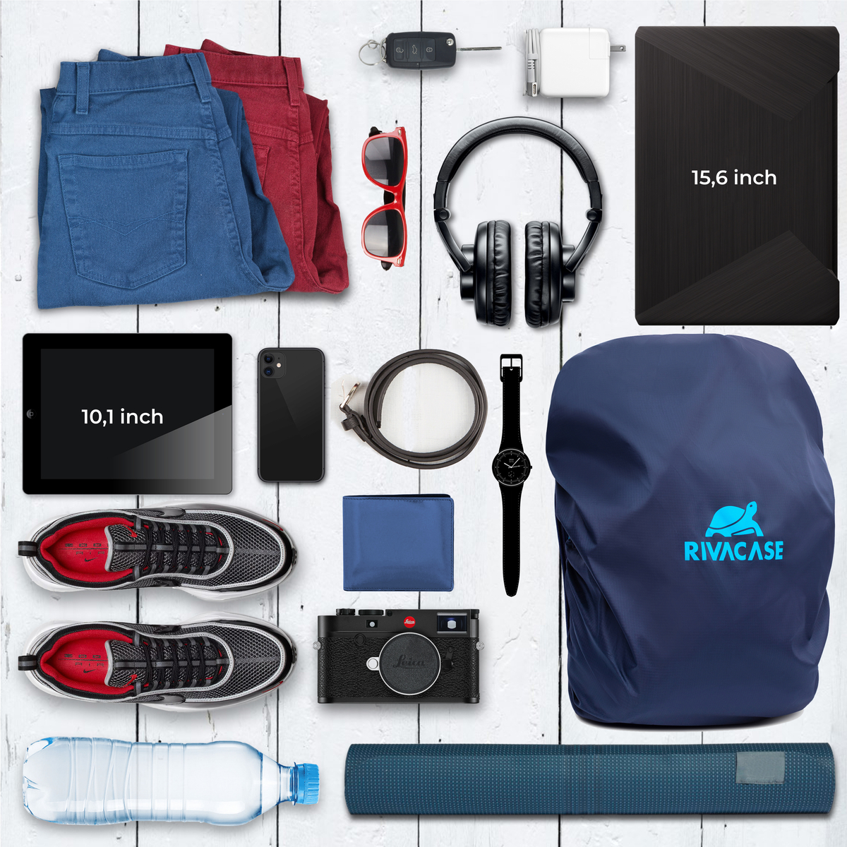 Vari oggetti su un tavolo bianco: jeans, occhiali da sole, cuffie, tablet, telefono, portafoglio, orologio, ecc.