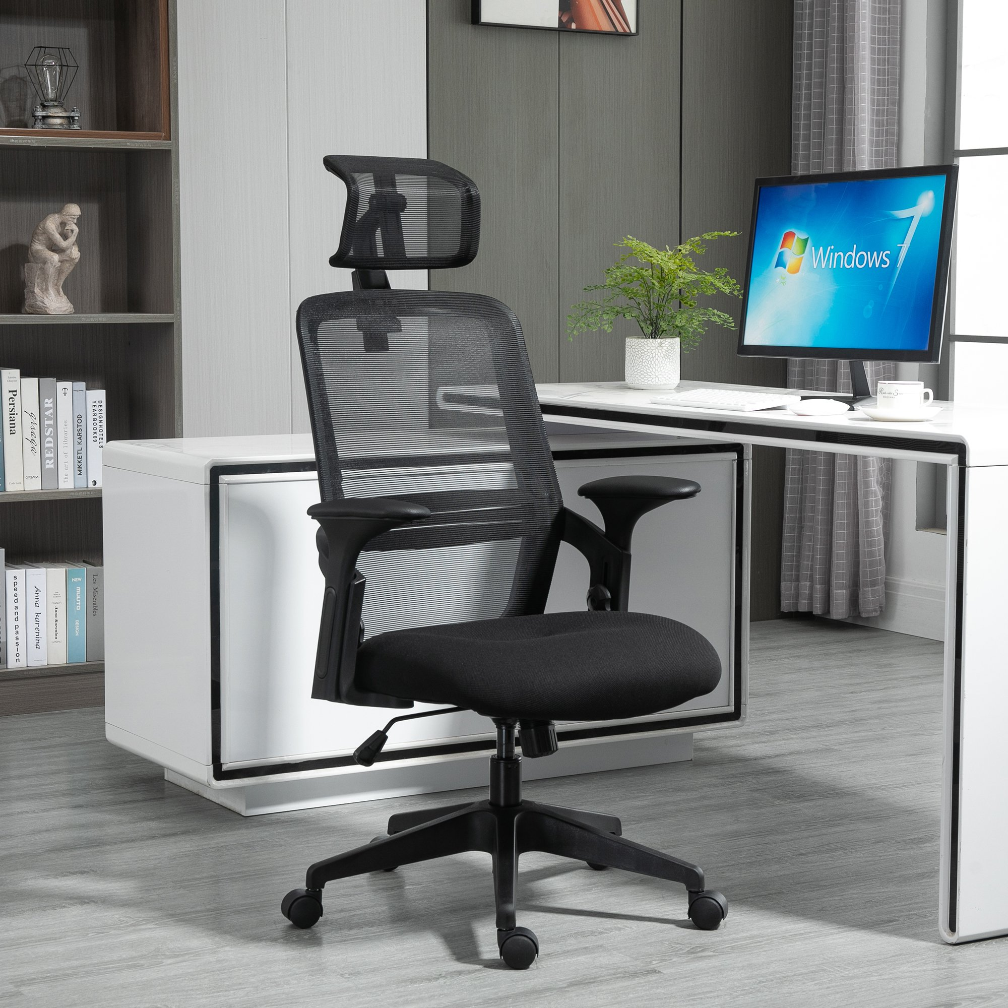 Silla de oficina negra con respaldo de malla en un entorno de oficina moderno. Visible una computadora y monitor.