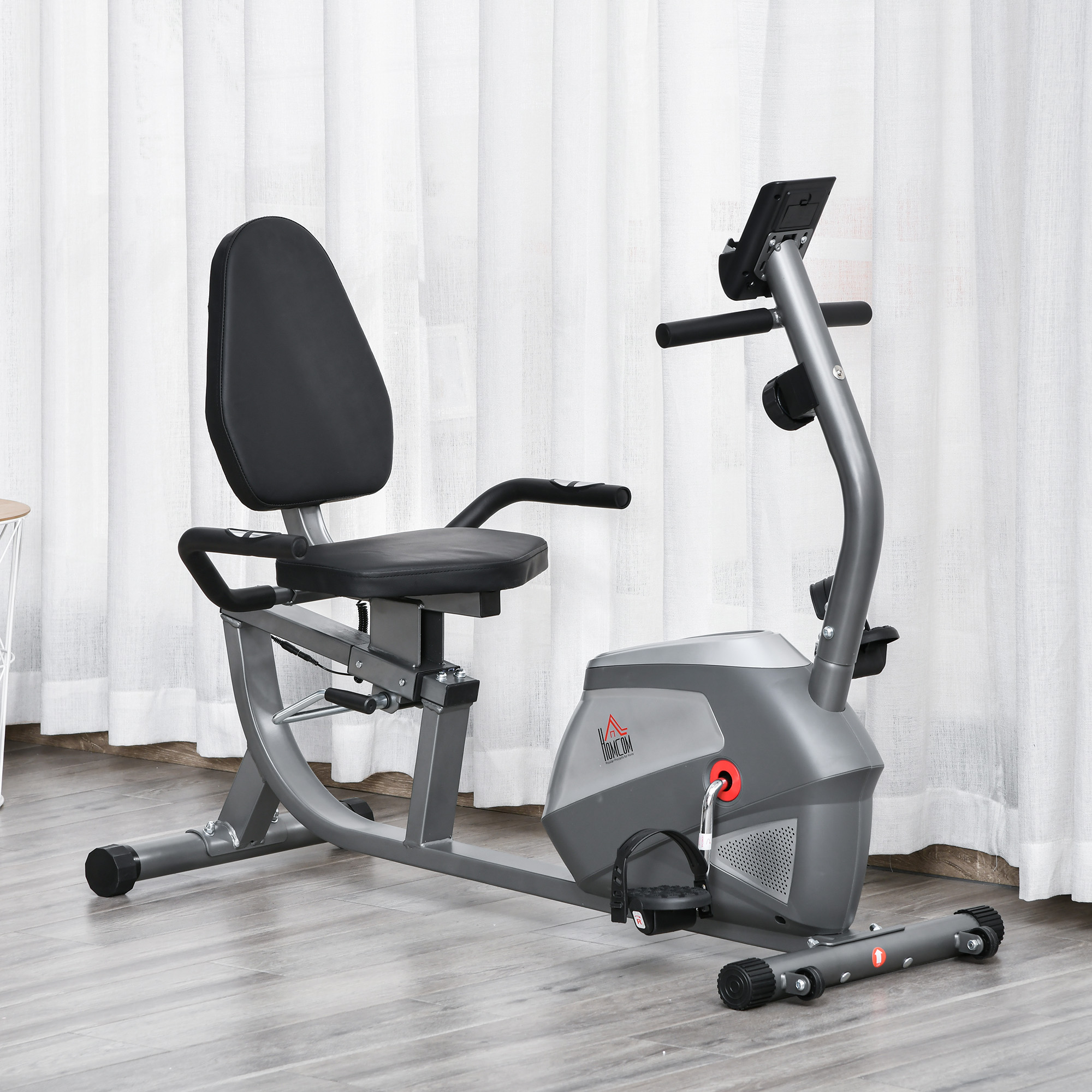 Una cyclette fissa. Corpo grigio, sedile e maniglie nere. Pavimento in legno chiaro.