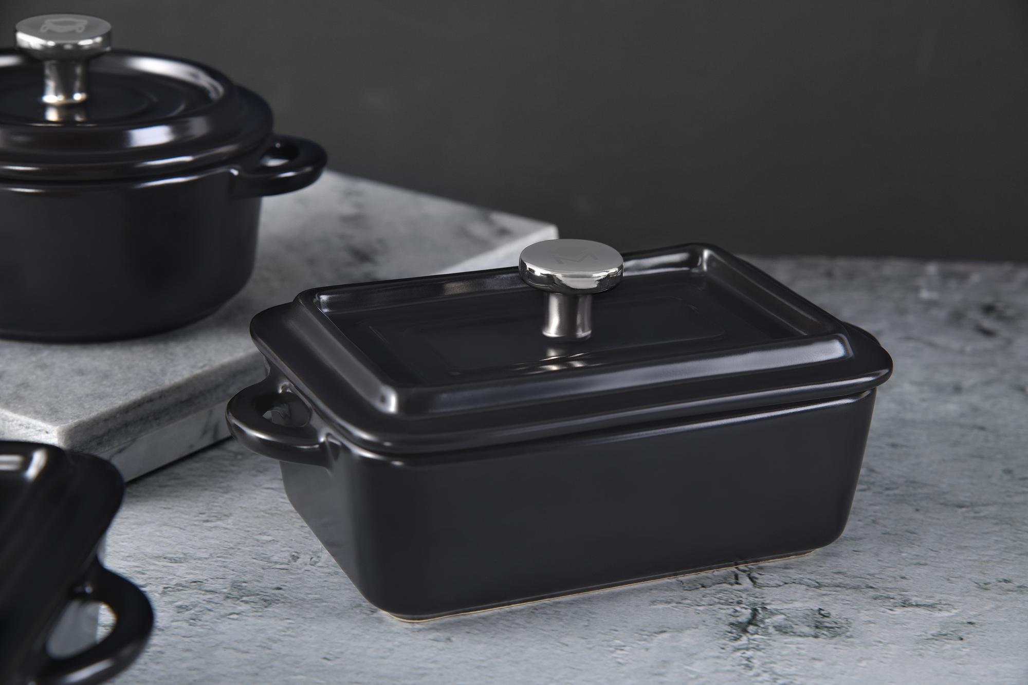 Plato de cerámica rectangular negro con pomo plateado en la tapa, sobre mármol.