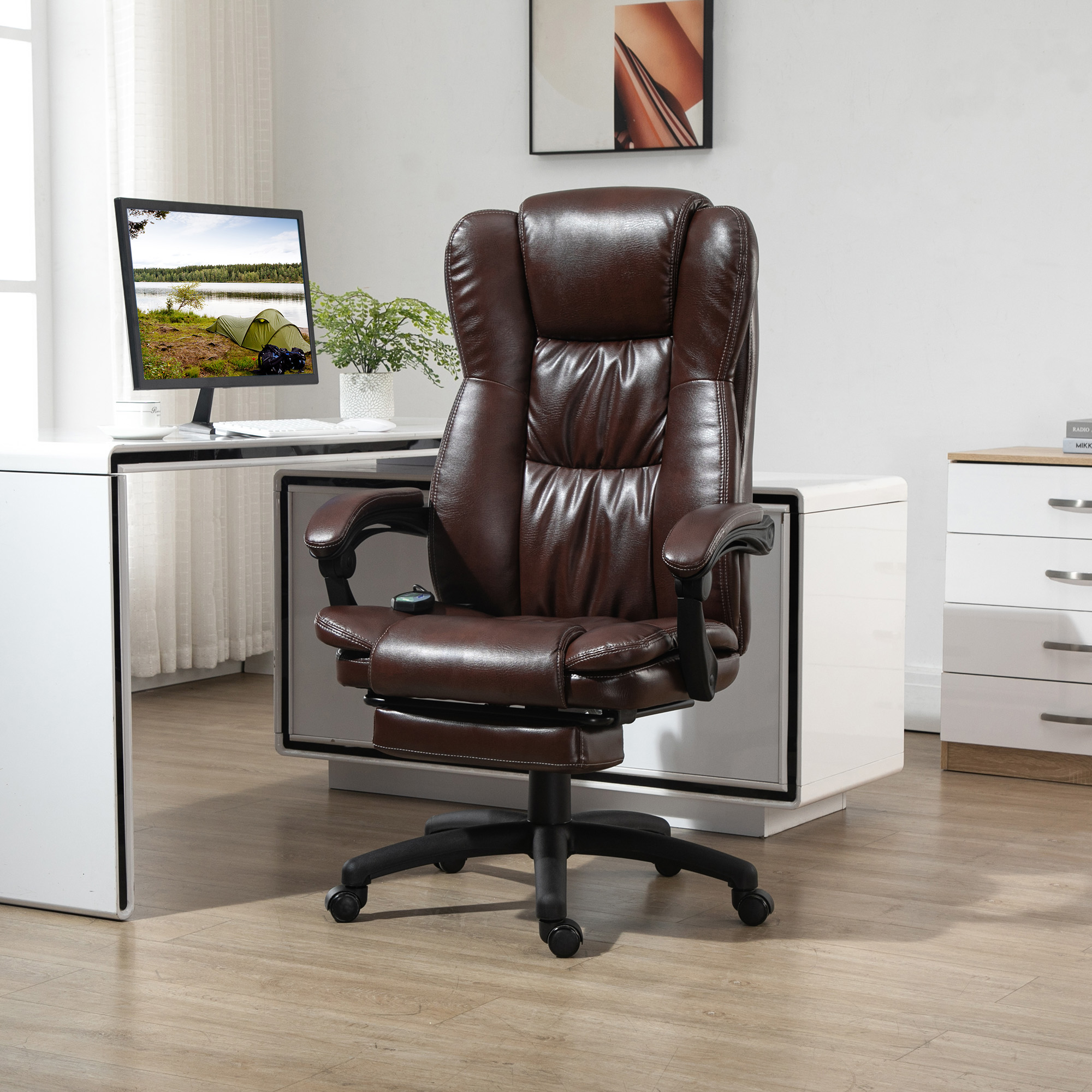 Una silla de oficina de cuero marrón con reposapiés, frente a un escritorio con monitor.