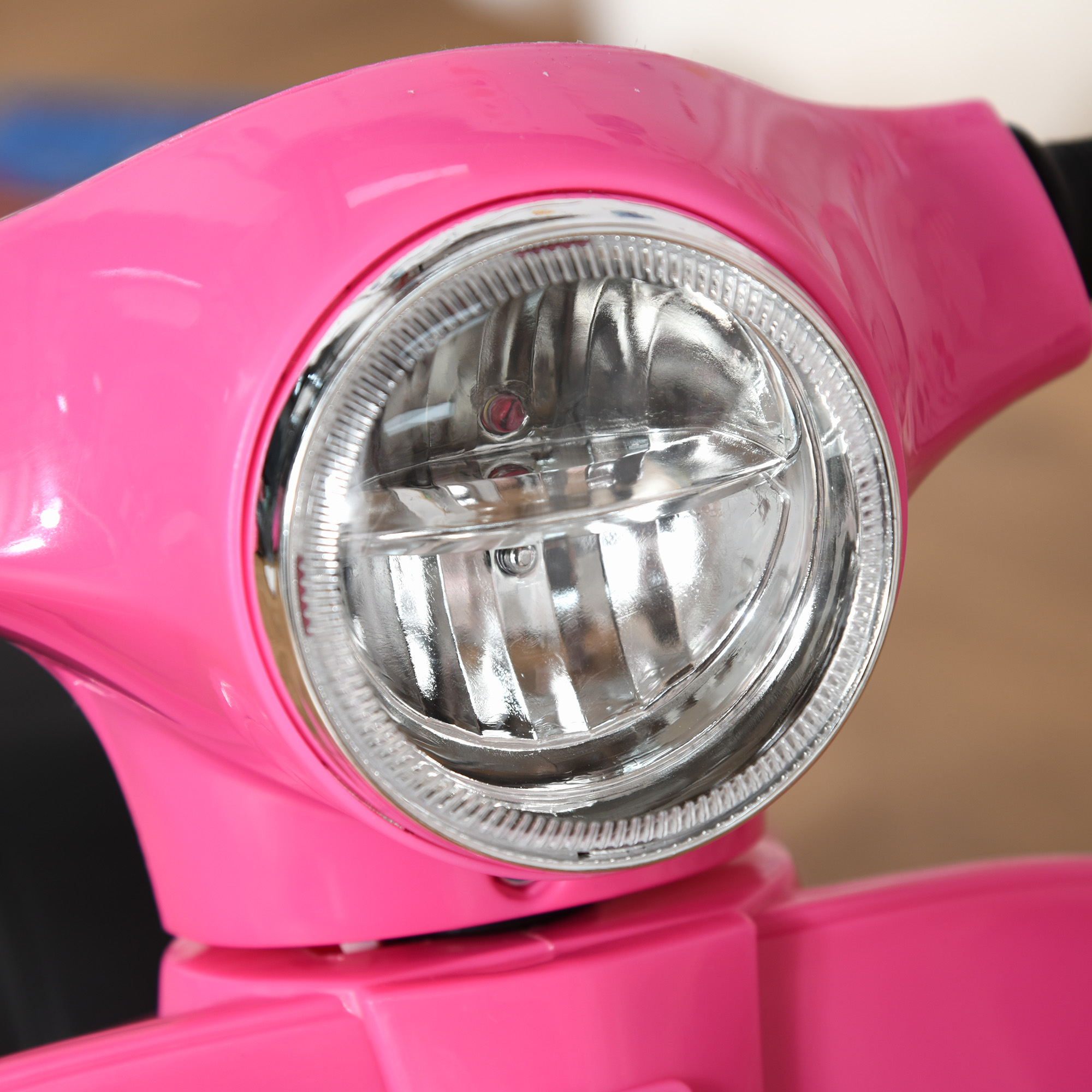 Primo piano del faro di uno scooter rosa. La finitura cromata circonda il vetro trasparente.