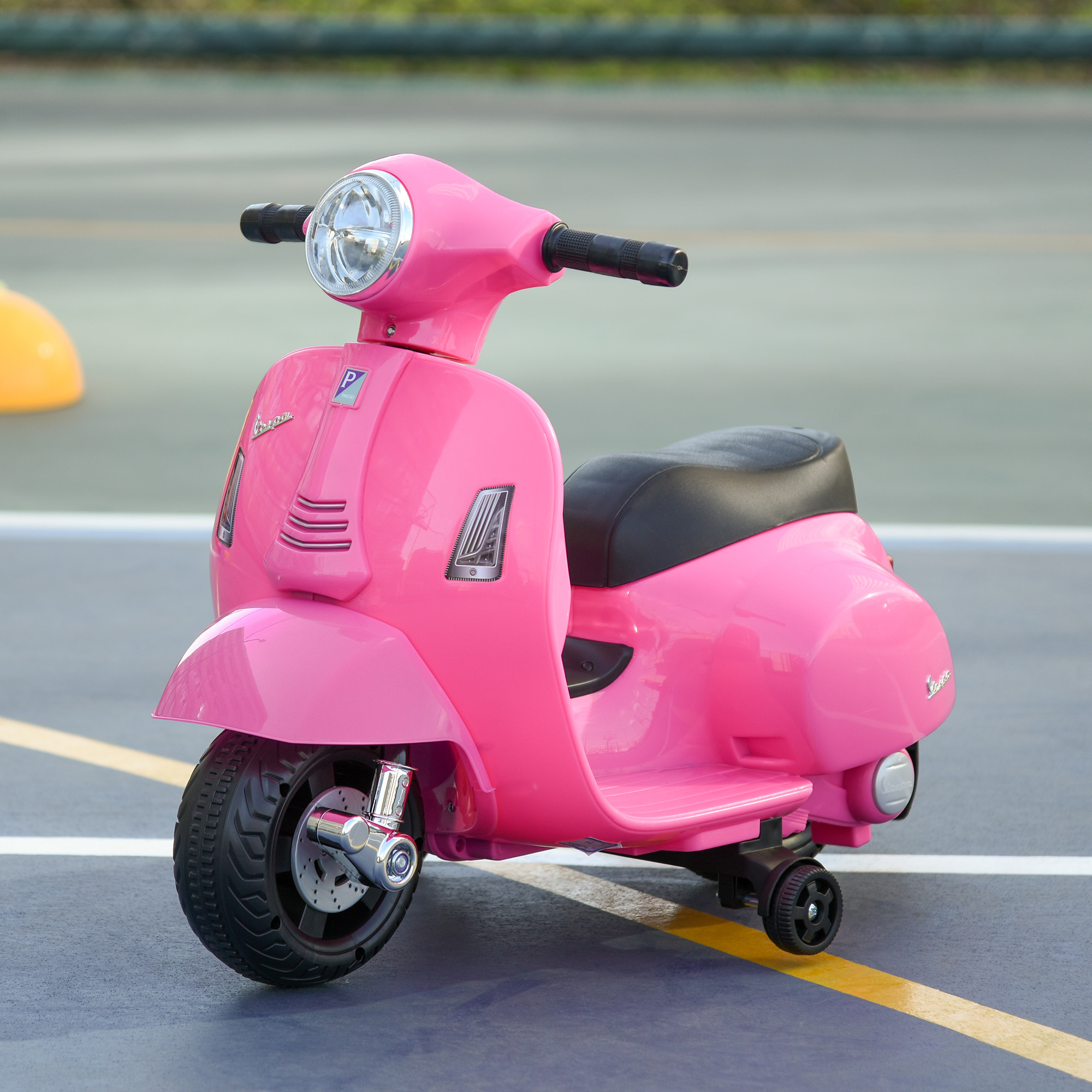 Un giocattolo scooter Vespa rosa con sedile nero, ruota anteriore grande, piccole ruote posteriori, su una superficie blu.