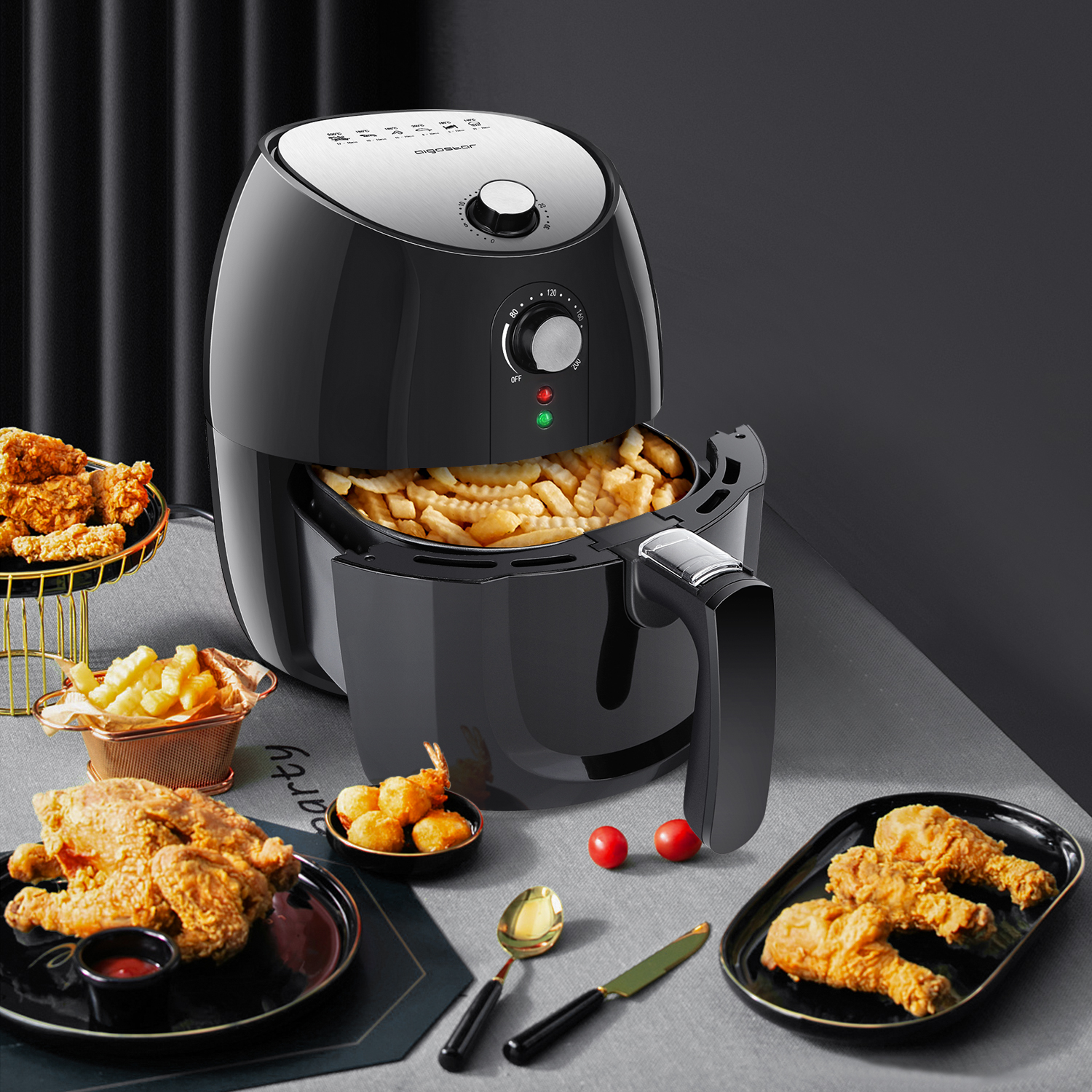 Freidora de aire negra con alimentos fritos. Pollo y papas fritas en la mesa, tomates y cubiertos rojos.