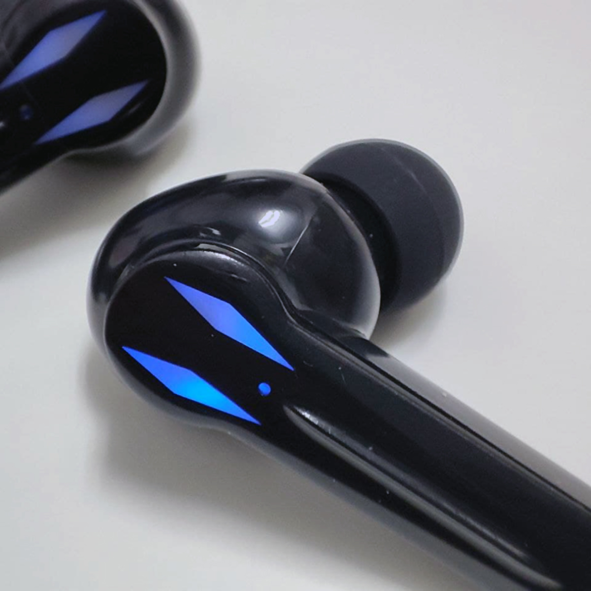 Primer plano de auriculares inalámbricos negros con detalles de luz azul sobre superficie blanca.