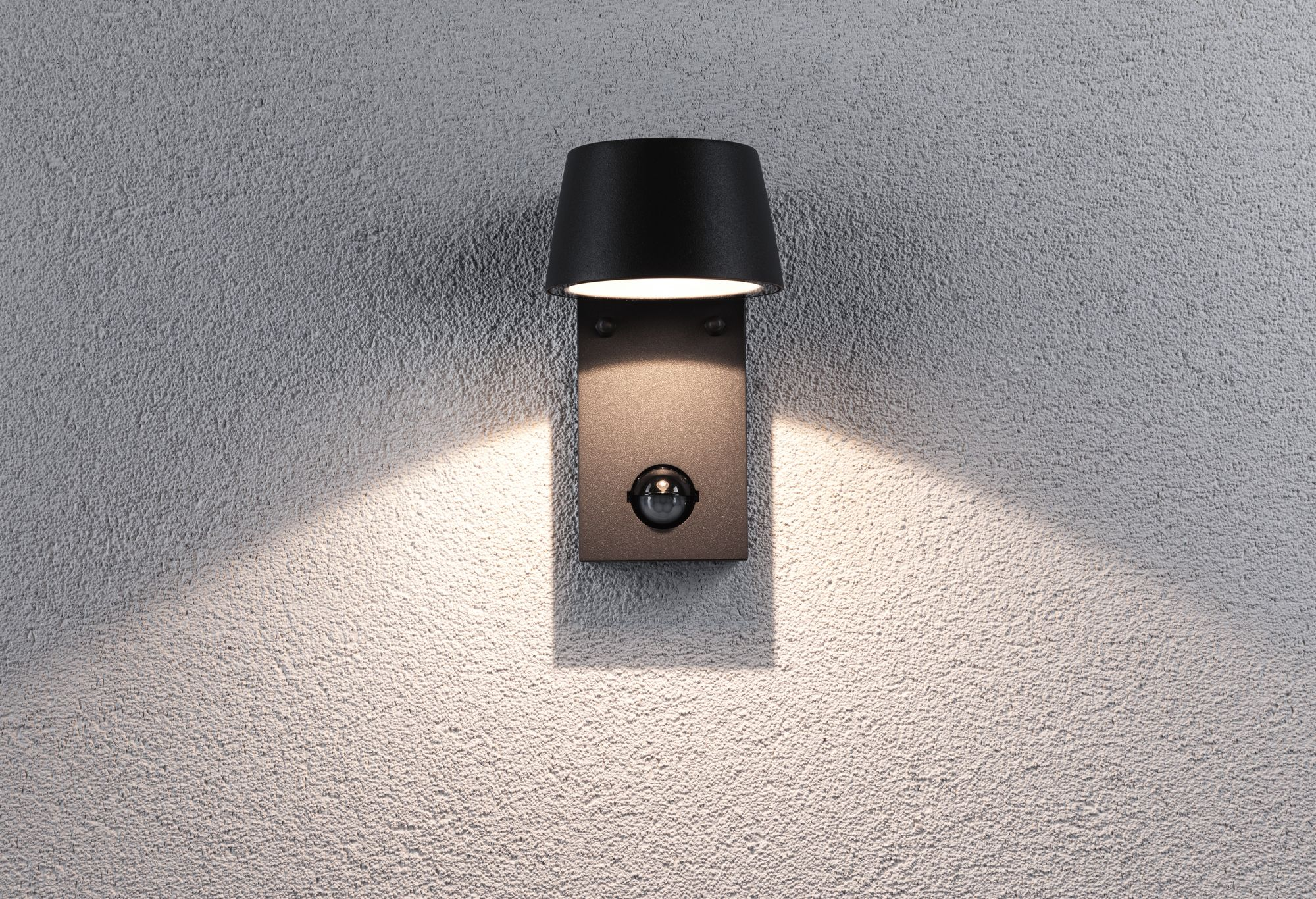 Czarna lampa ścienna z czujnikiem ruchu. Światło świeci w dół.