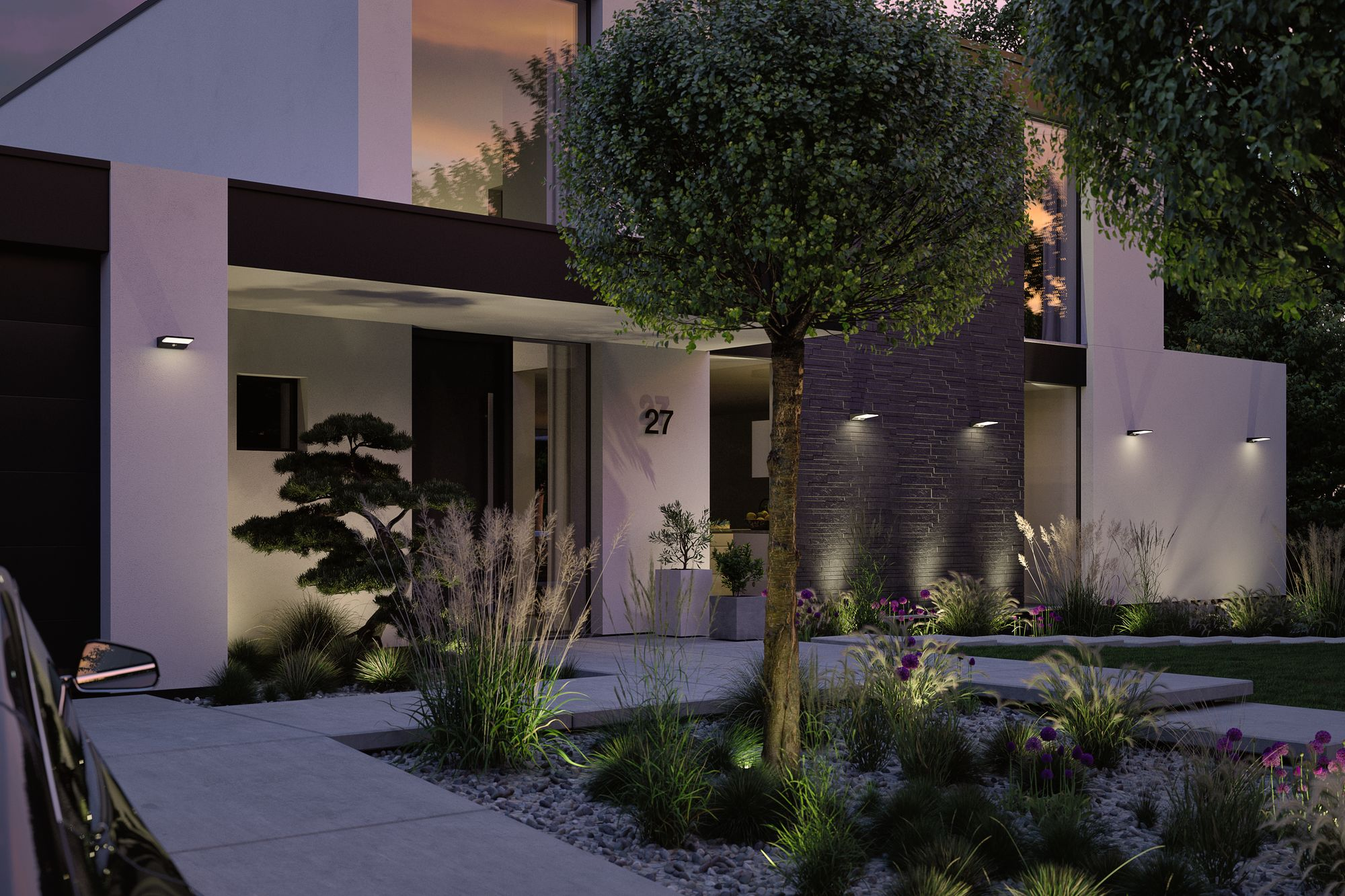Nowoczesny dom o zmierzchu, oświetlony światłami zewnętrznymi. Krajobraz obejmuje rośliny, drzewa i podjazd.