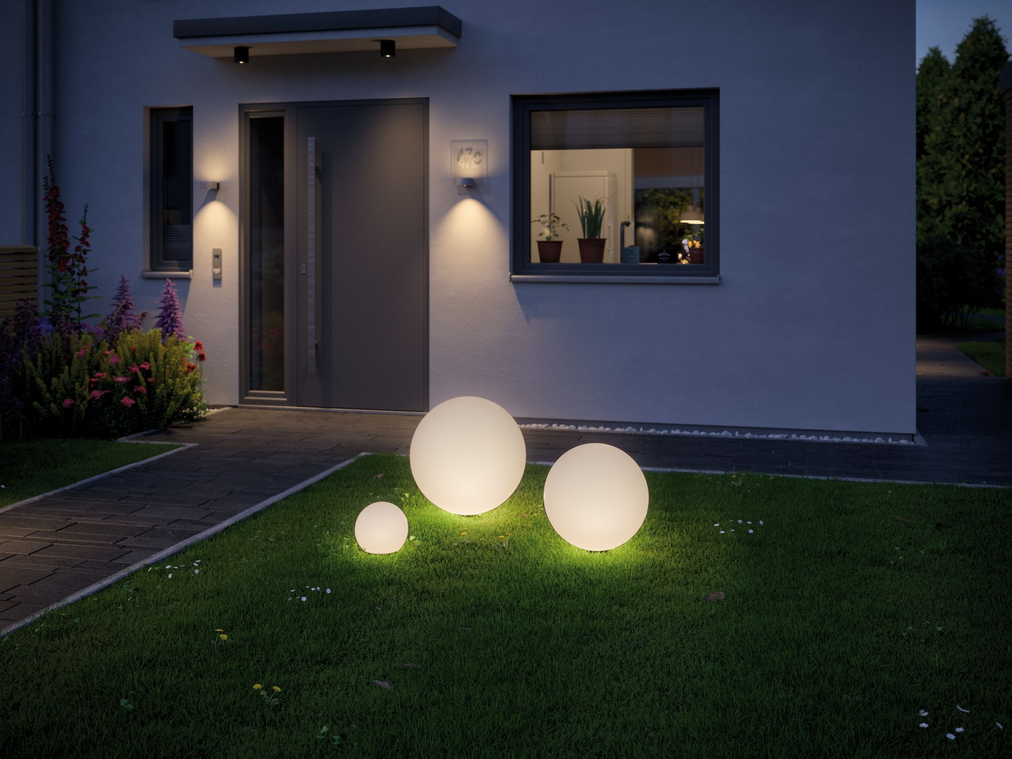 Un esterno di casa di notte con tre luci a globo illuminate in un cortile. La casa ha le luci accese.
