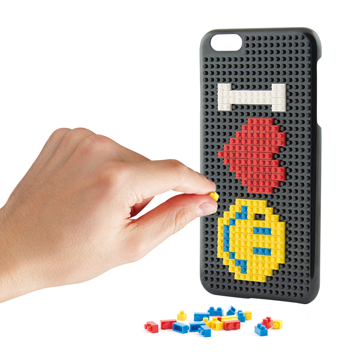Persona che posiziona un mattone giallo su una custodia con un design pixelato. Altri mattoni sparsi.