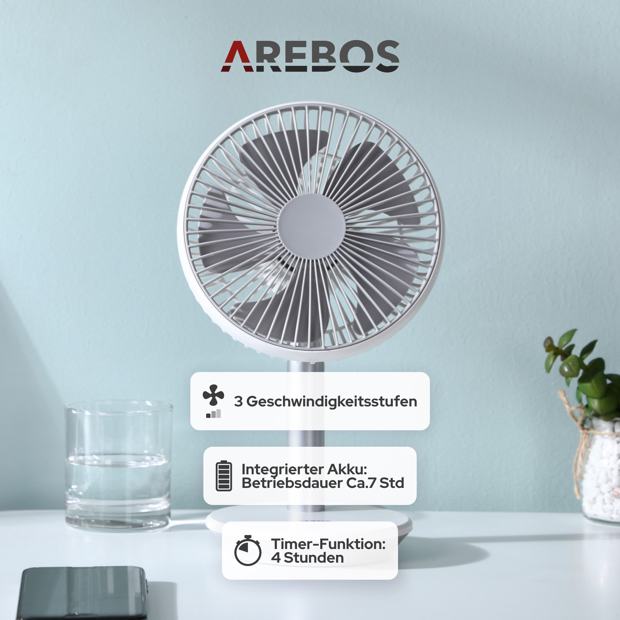 Ein weiß-grauer Ventilator mit drei Geschwindigkeitsstufen und Timerfunktion, sowie ein Wasserglas auf dem Tisch.