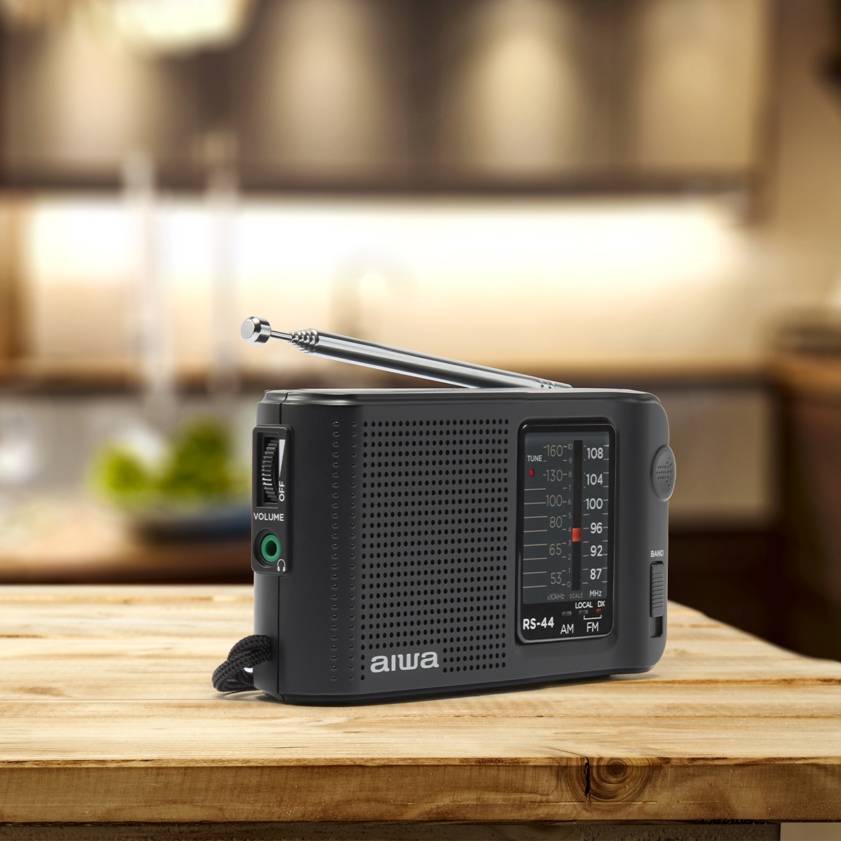 Czarny radio Aiwa na drewnianej powierzchni. Posiada pokrętło strojenia i kratkę głośnika.