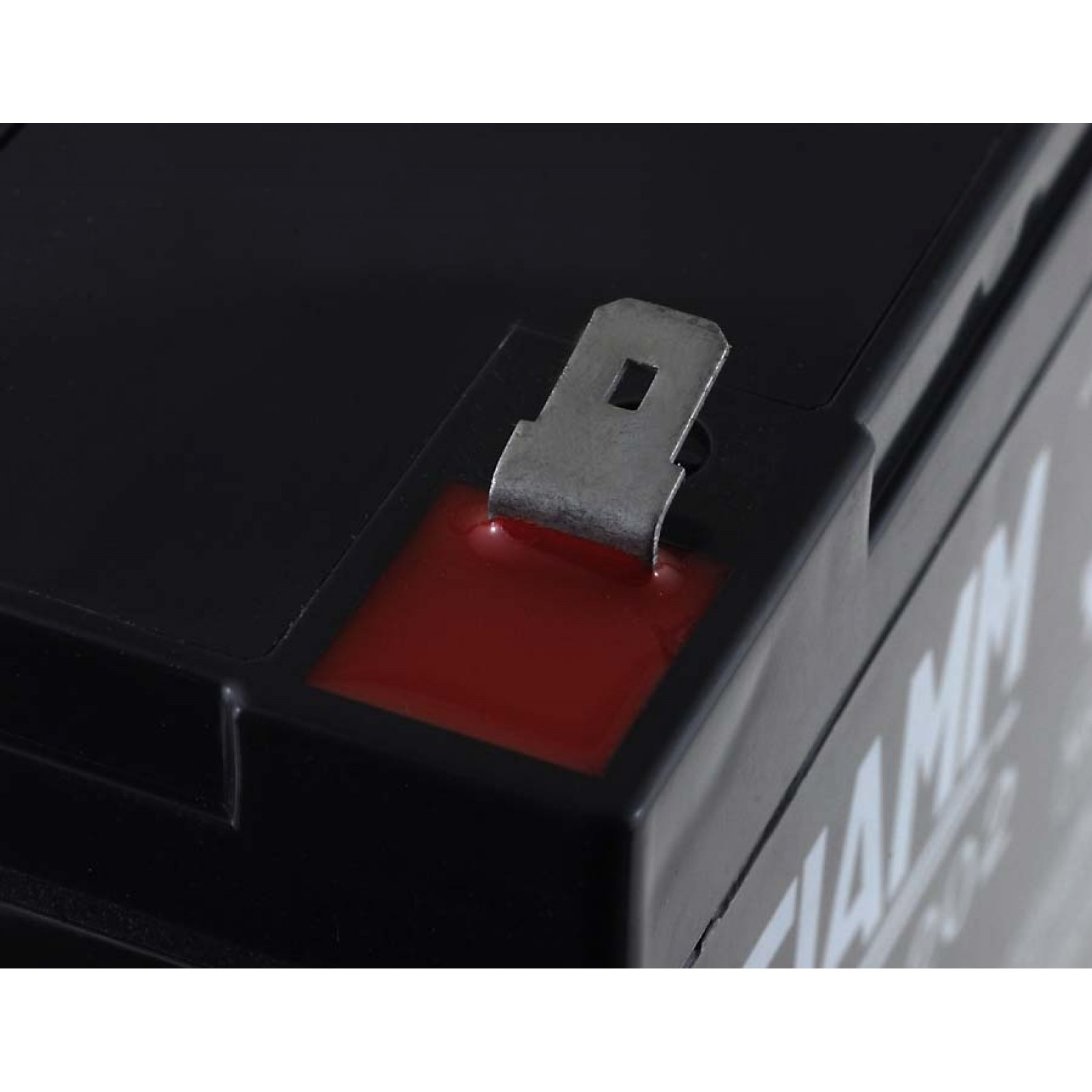 Terminal de batería negro con sellador rojo. El terminal tiene un clip metálico.
