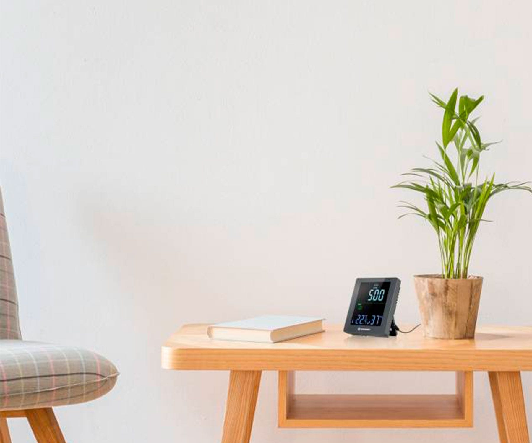 Mesa de madera con planta, reloj digital y libro. Silla a la izquierda. Fondo blanco.