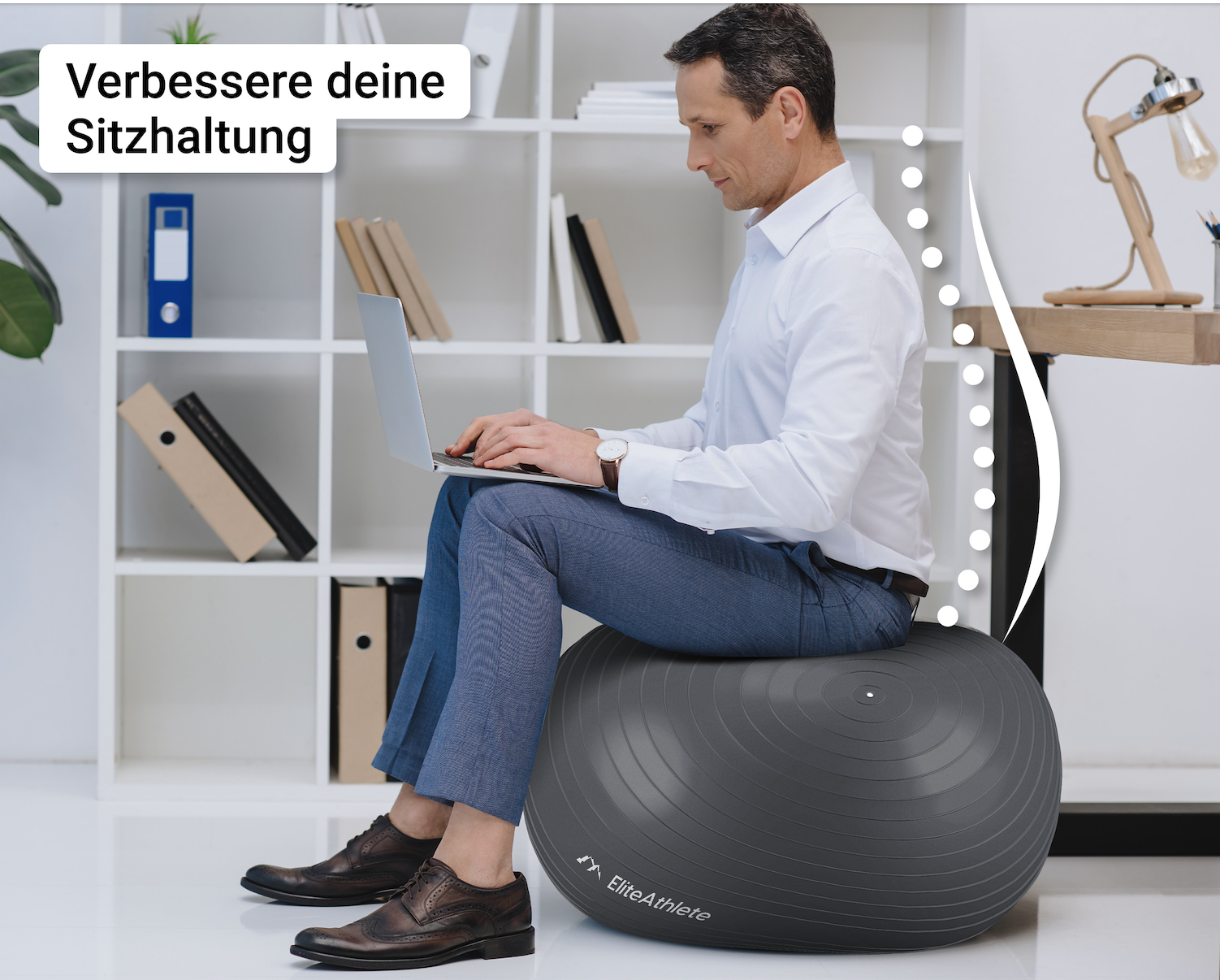Ein Mann sitzt auf einem grauen Gymnastikball an einem Schreibtisch und benutzt einen Laptop. Im Hintergrund ein Regal mit Gegenständen.