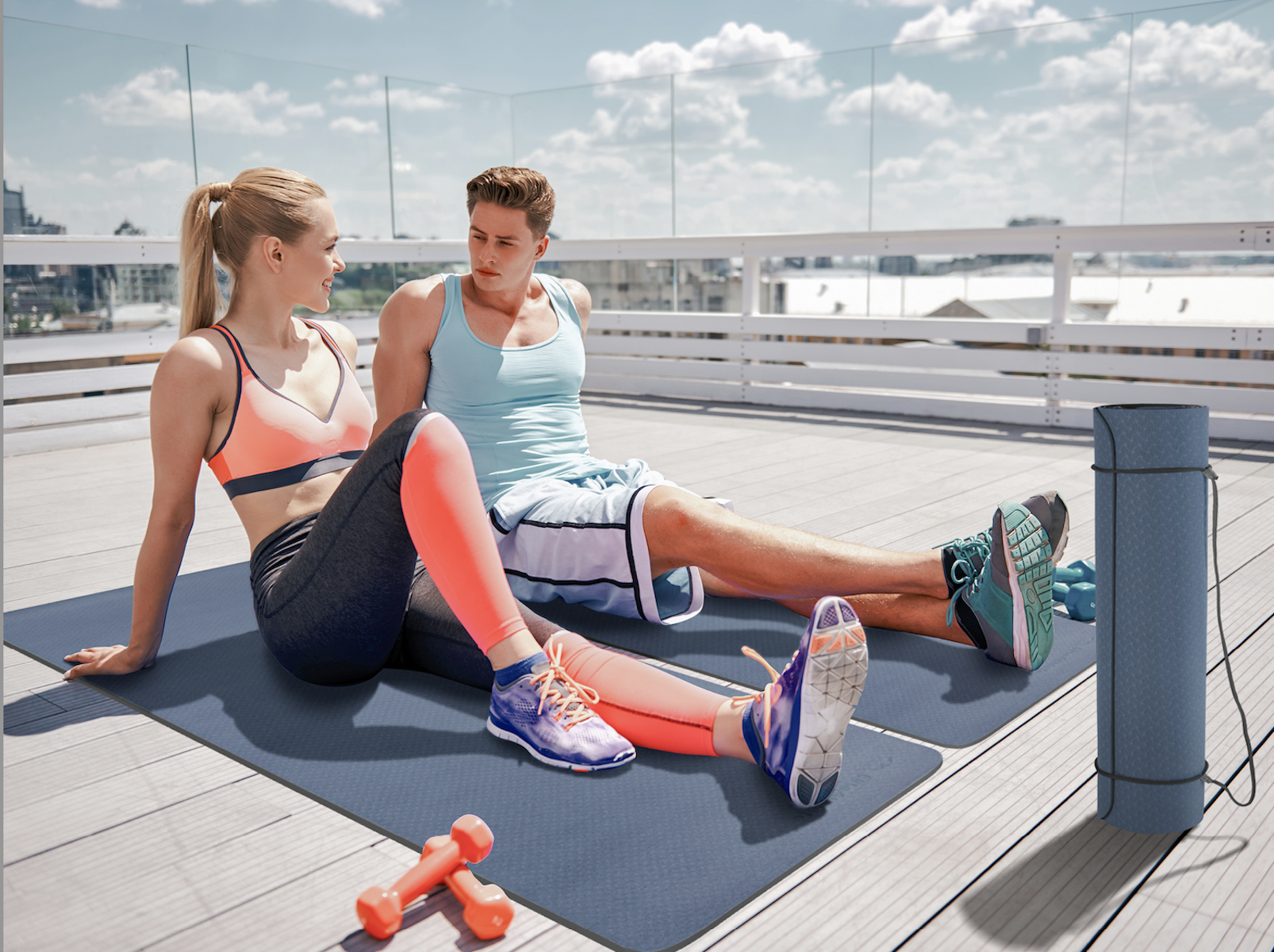 Zwei Personen sitzen draußen auf blauen Matten, mit Yogamatte und Gewichten.