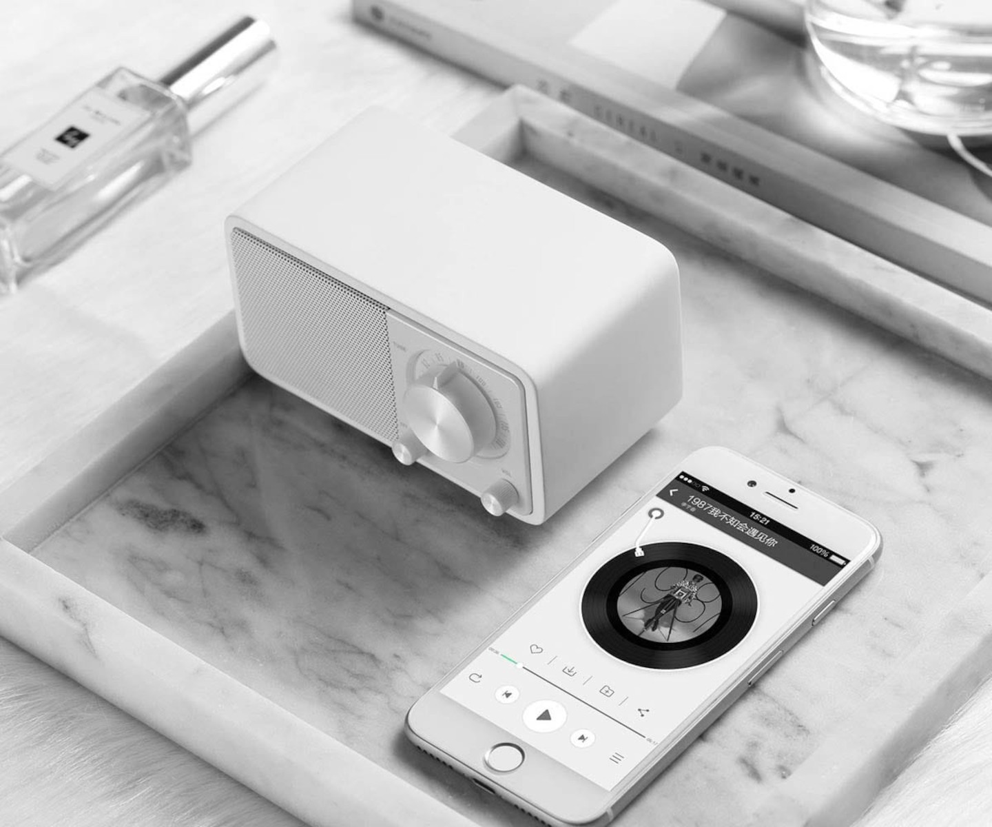 Białe radio i telefon na tacy. Telefon pokazuje kontrolki muzyki. Perfumy w tle.