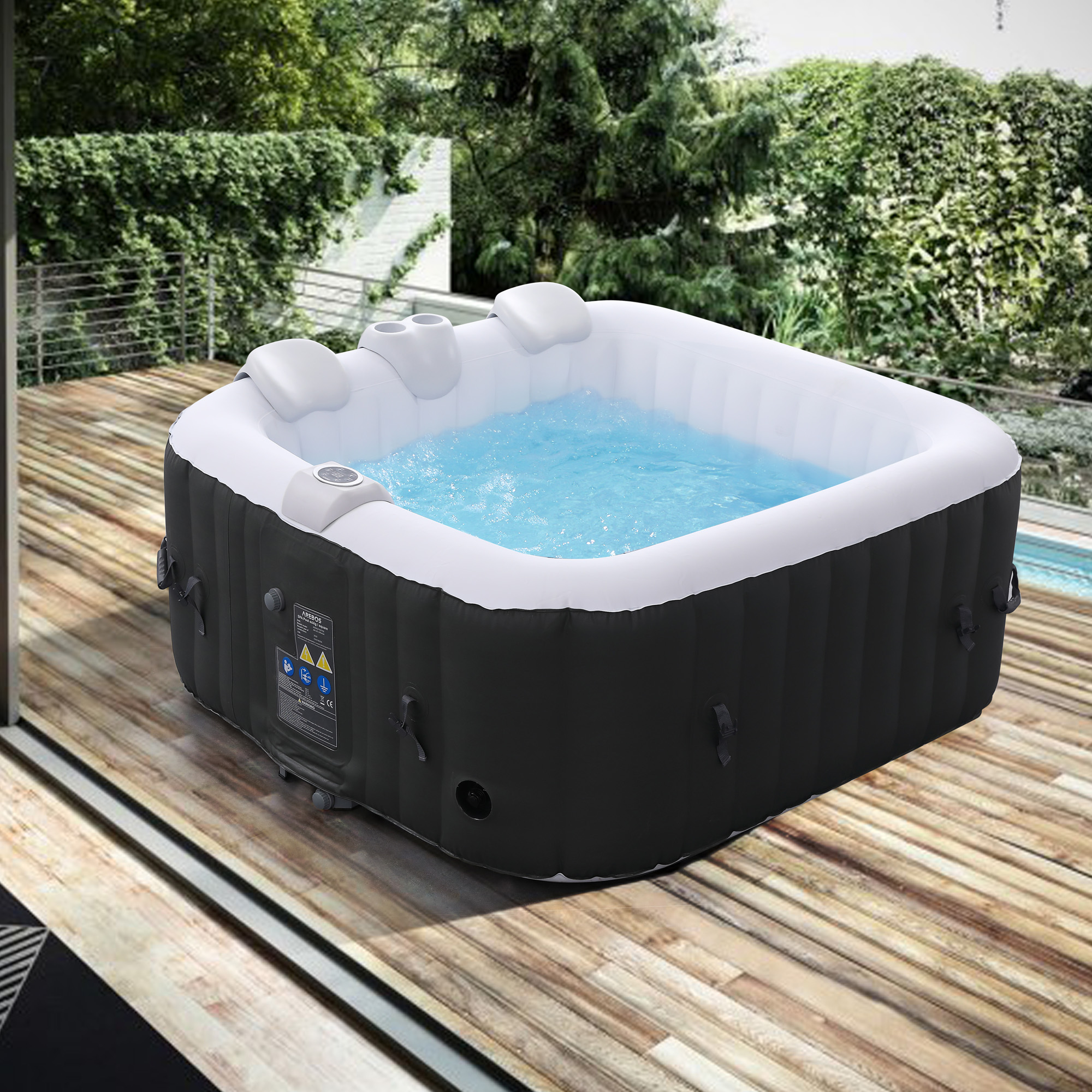 Quadratischer Whirlpool mit Wasser, Düsen und Bedienelementen auf Holzterrasse. Bäume im Hintergrund.