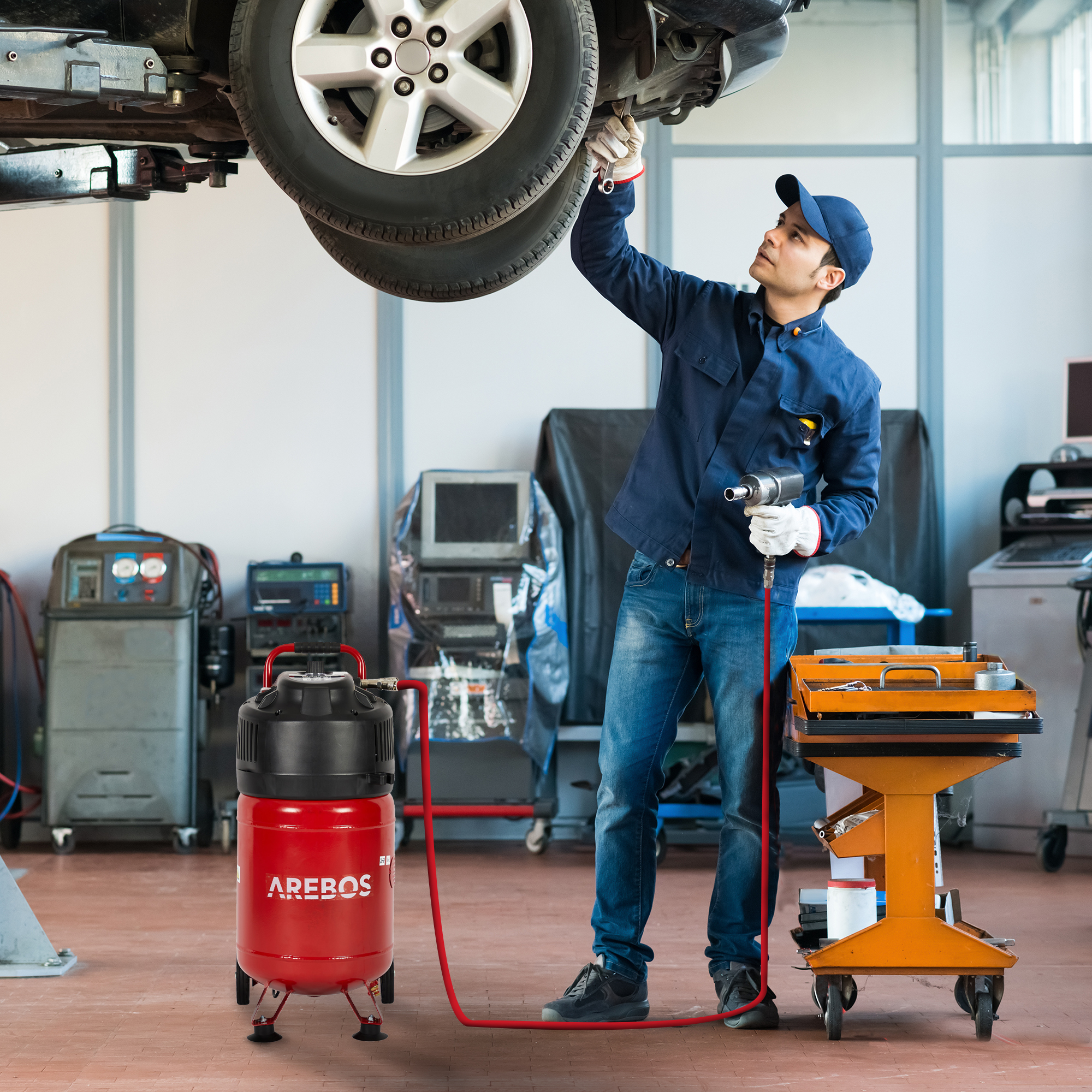 Ein Mechaniker arbeitet an einem Auto, daneben roter Luftkompressor.