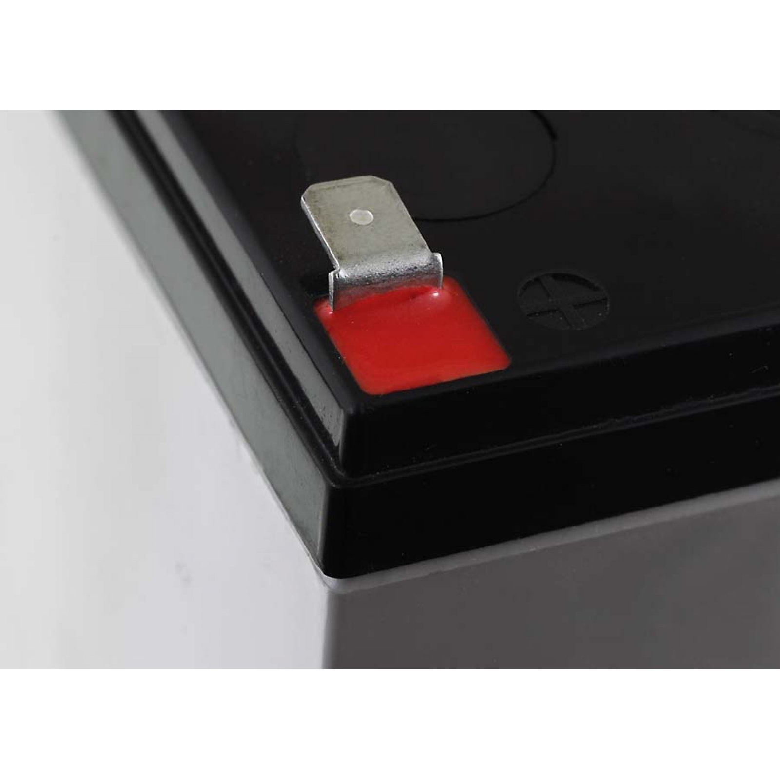 Batería rectangular negra con rectángulo rojo y conector metálico.