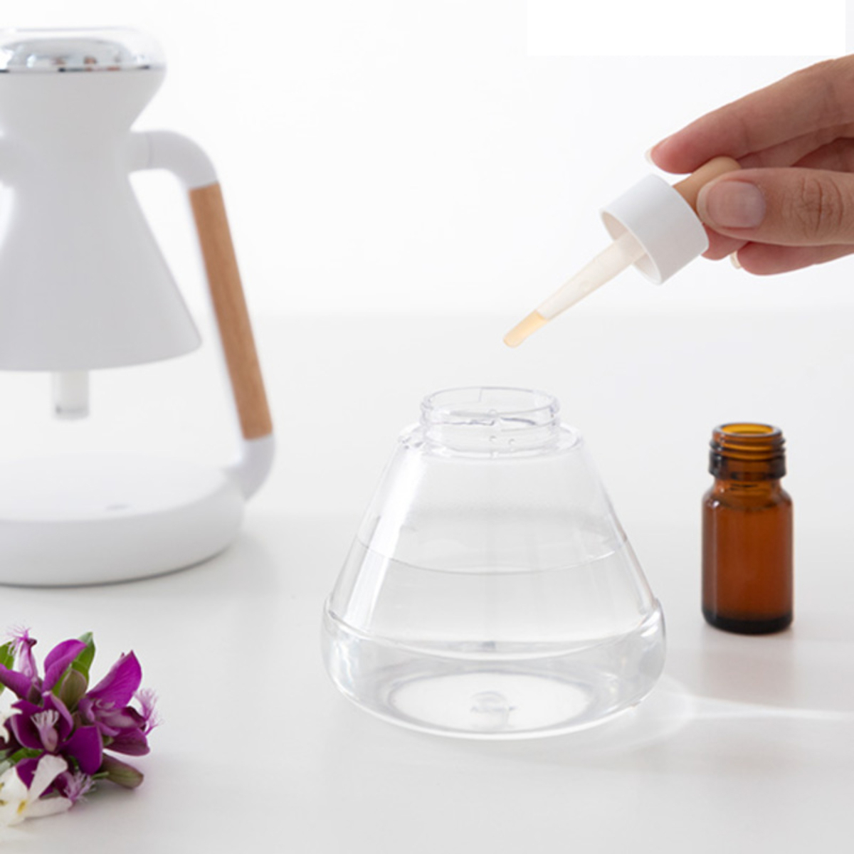Eine Hand gießt Flüssigkeit aus einer Pipette in einen transparenten Behälter. Ein weiterer weißer Spender ist sichtbar.