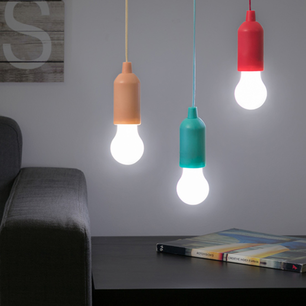 Tres luces colgantes. Cada una tiene un color diferente: naranja, verde y rojo. Sobre un fondo oscuro.