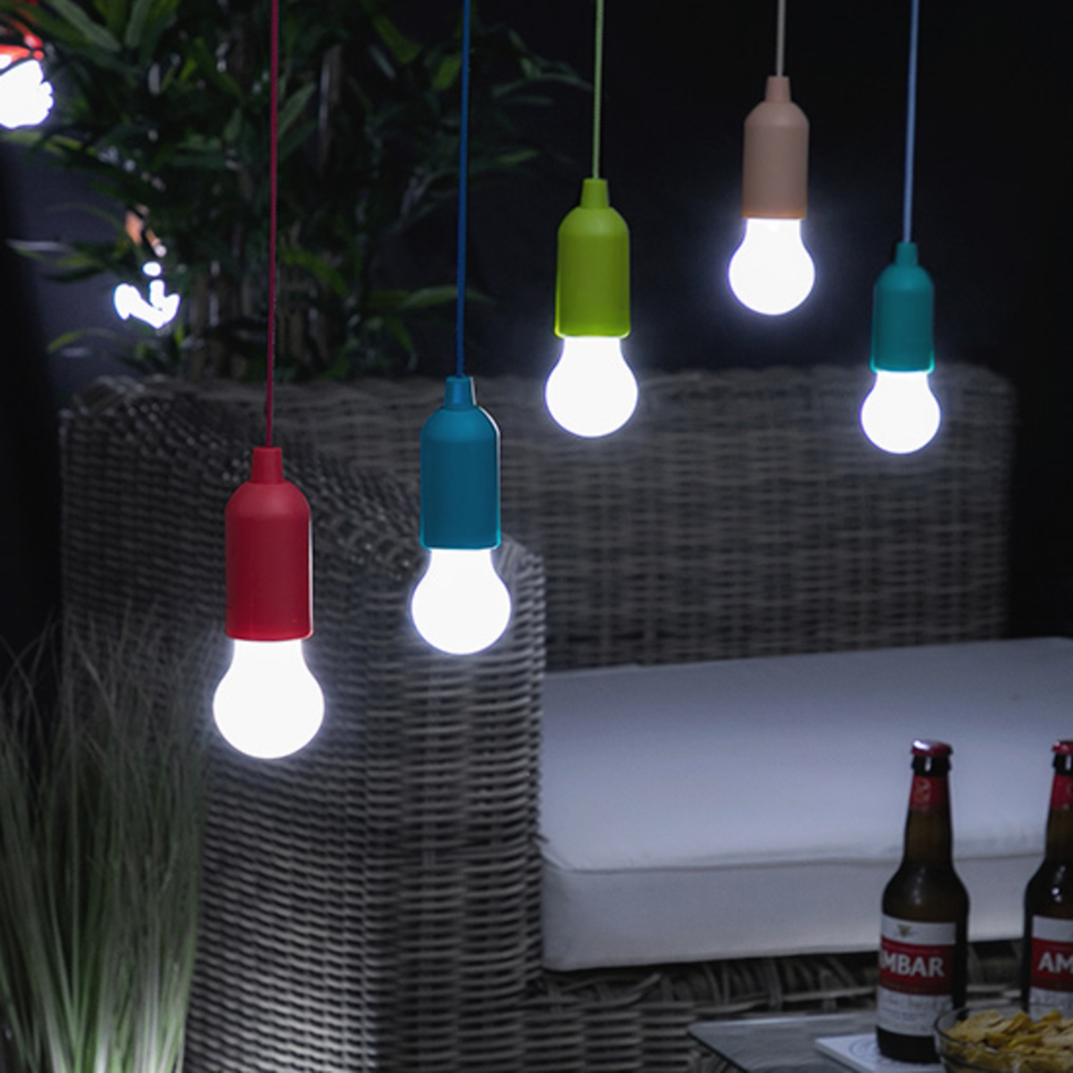 Escena al aire libre con luces colgantes coloridas y botellas de cerveza. Una silla de mimbre en el fondo.
