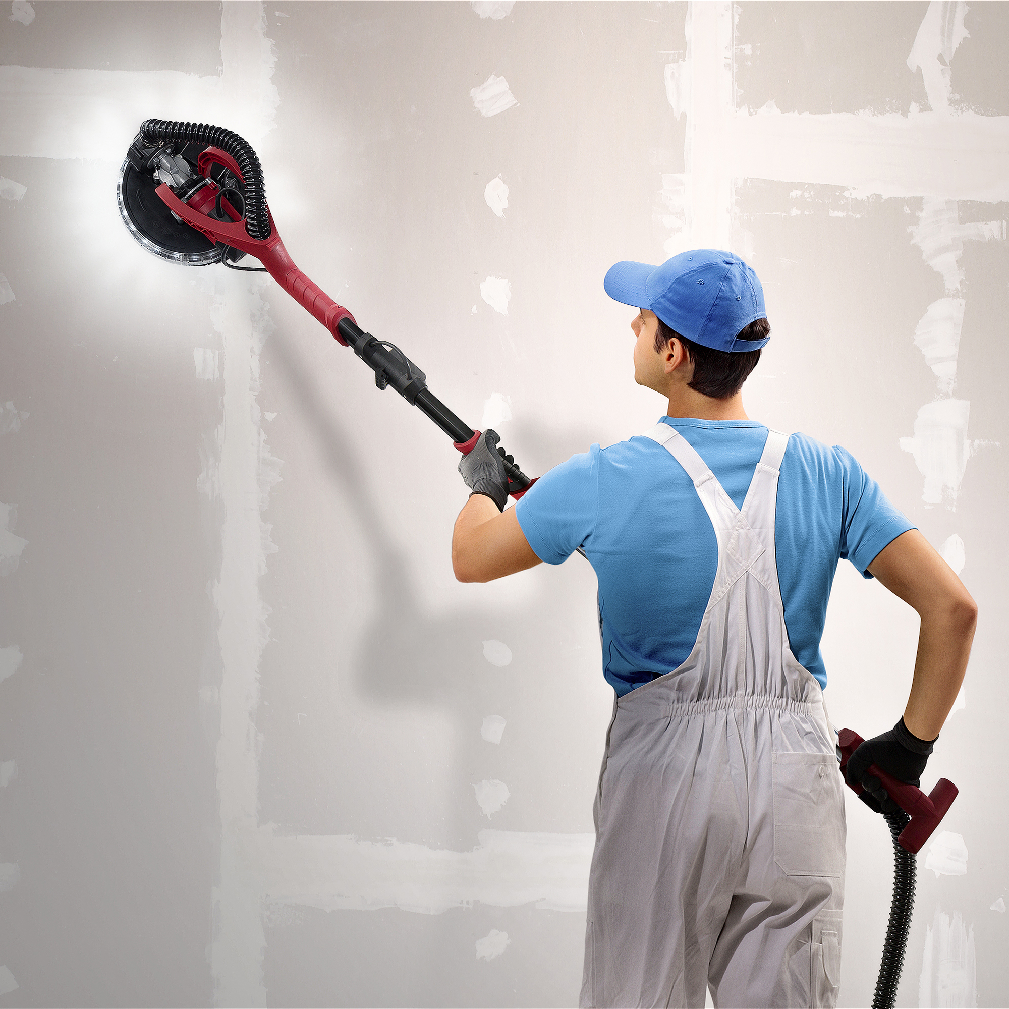Person in Overalls schleift mit einem roten Schleifwerkzeug eine Wand.