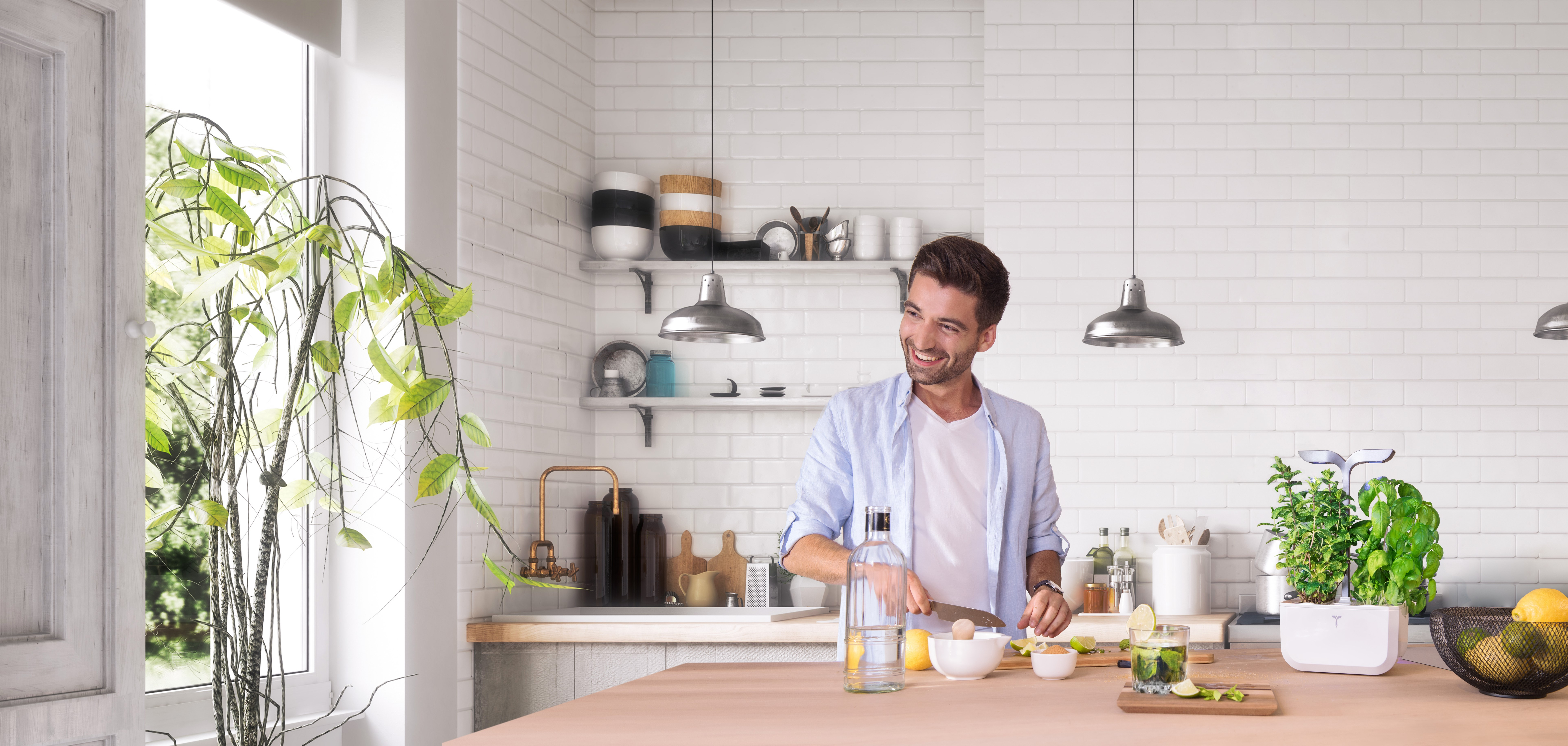 Un uomo sorride in una cucina luminosa, preparando una bevanda con limoni ed erbe aromatiche.