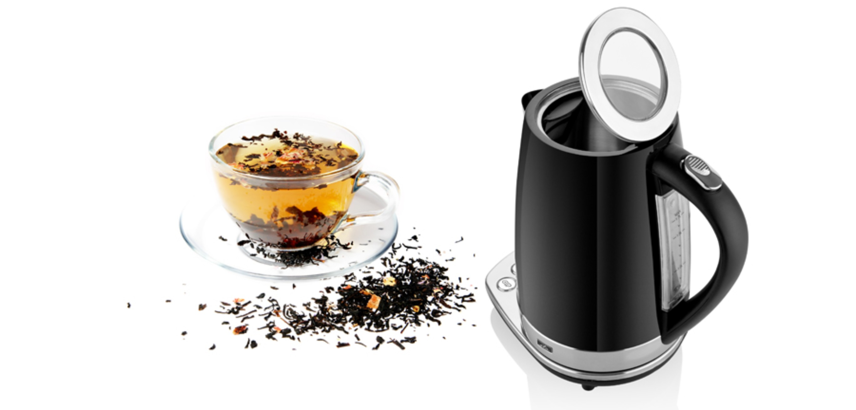 Schwarzer Wasserkocher mit einer Teetasse und losen Teeblättern auf weißer Oberfläche verstreut.