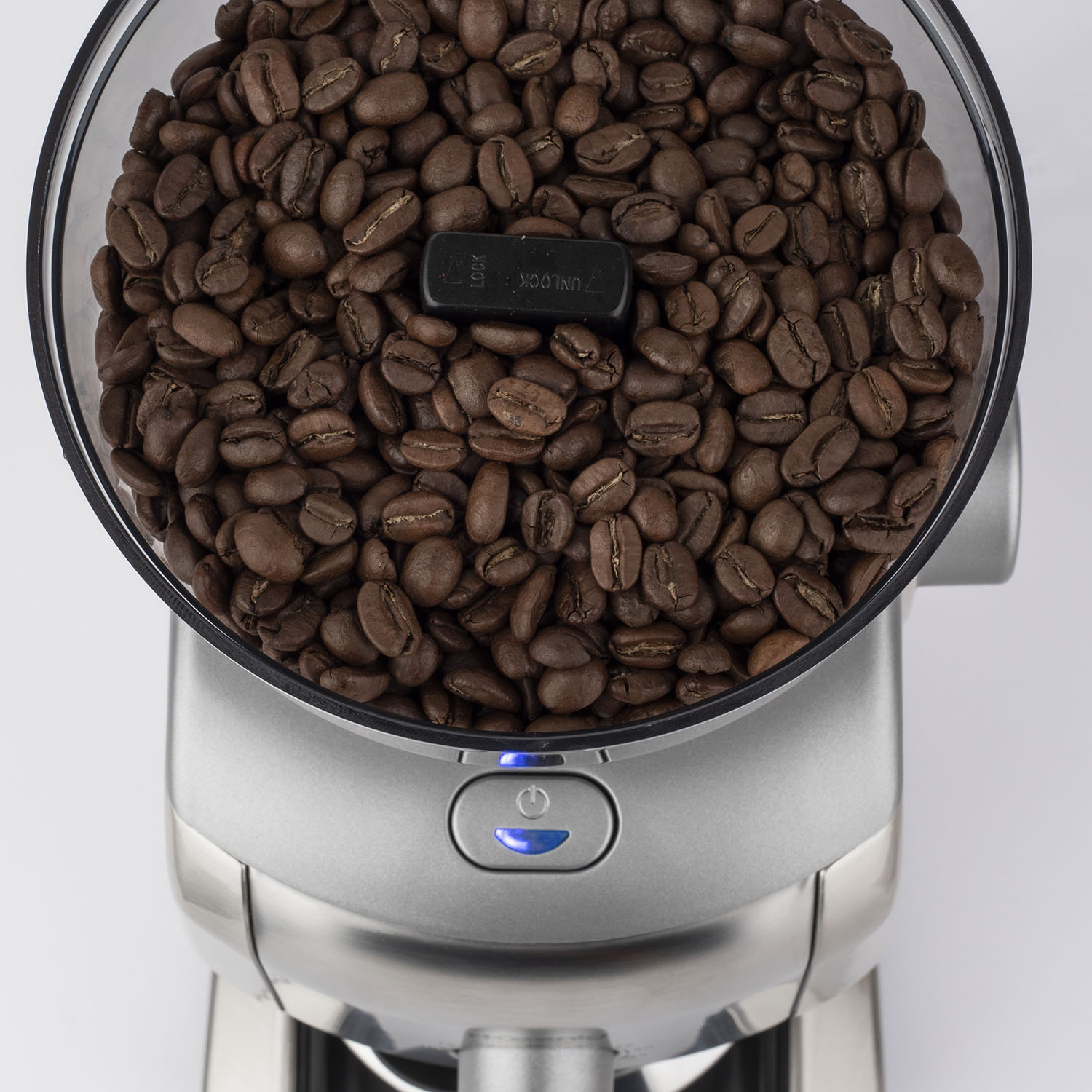 Chicchi di caffè in un macinacaffè. Il macinacaffè è argentato e i chicchi marroni.