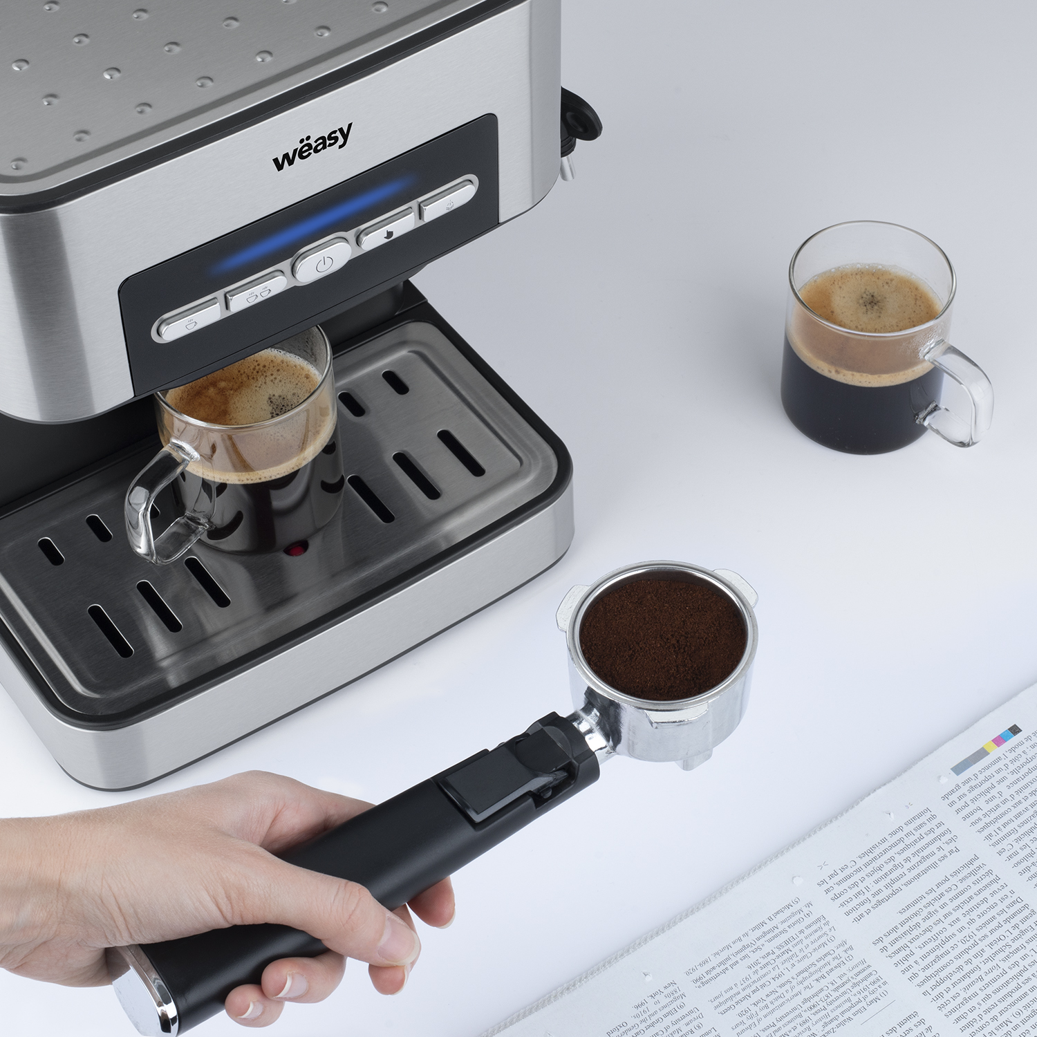 Espressomaschine mit zwei klaren Glasbechern, die mit Kaffee gefüllt sind. Hand hält einen Siebträger mit Kaffeesatz.