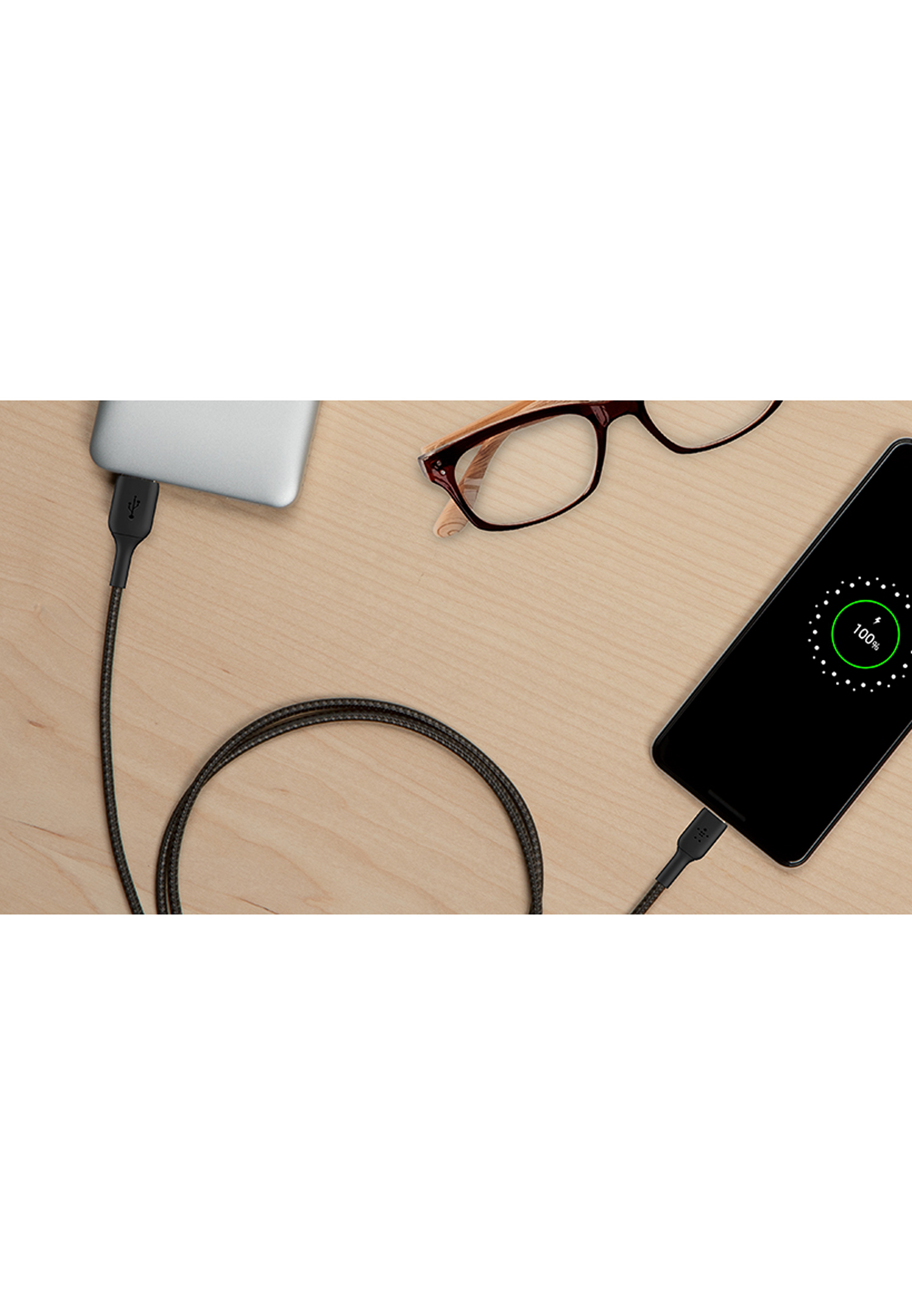 Laptop e smartphone collegati con un cavo, occhiali, su un tavolo di legno.