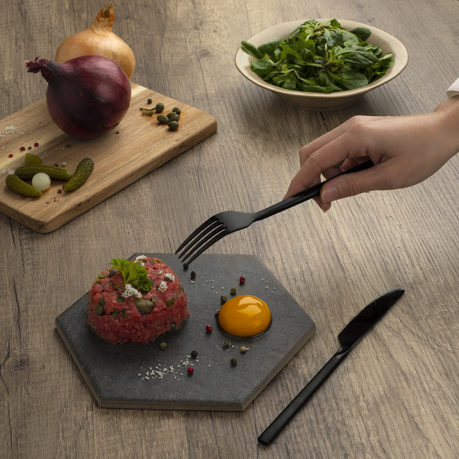 Un tavolo con cibo. C'è tartare di manzo, un tuorlo d'uovo, cipolle e verdure.