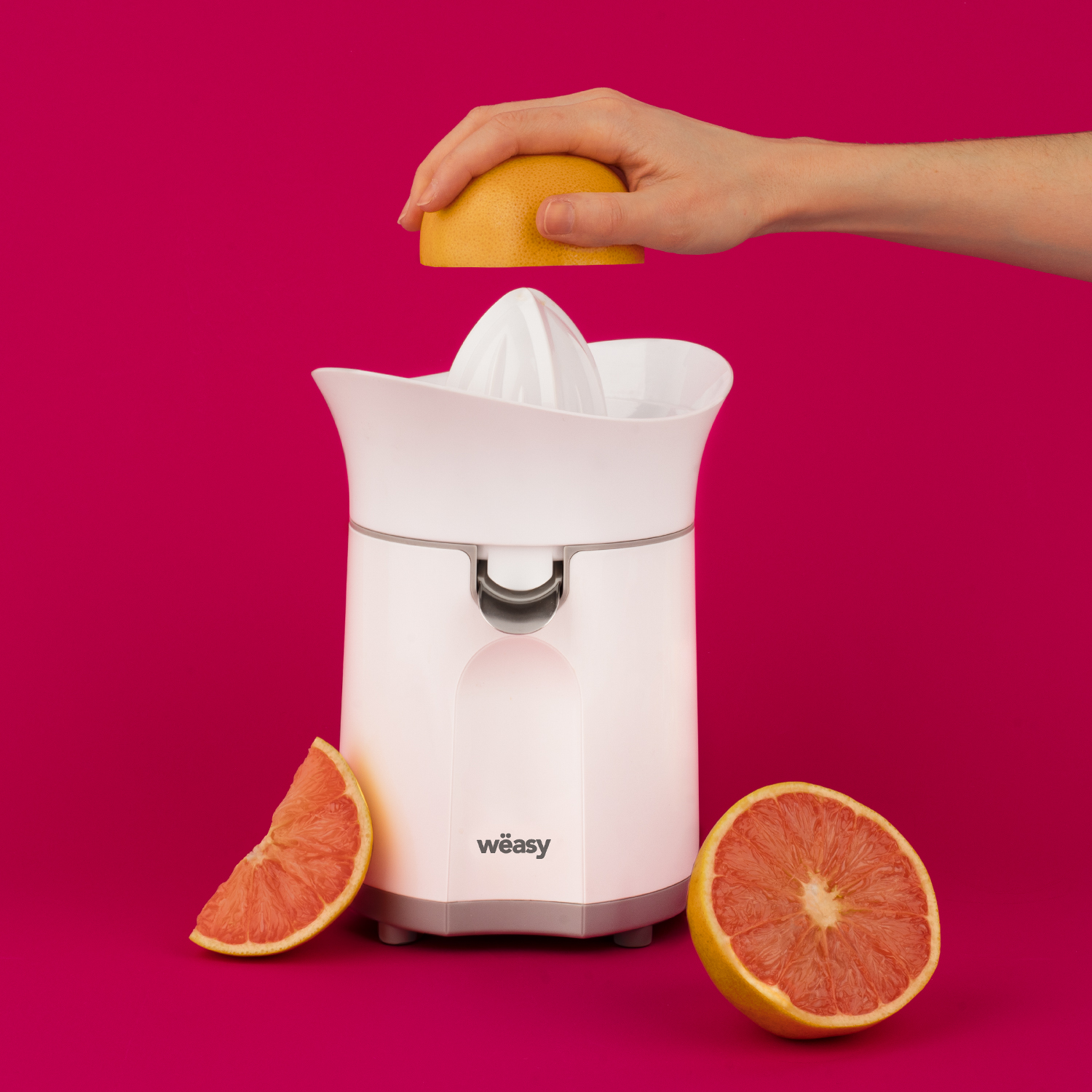 Exprimidor eléctrico blanco con pomelo. Mano sostiene mitad de pomelo sobre exprimidor.