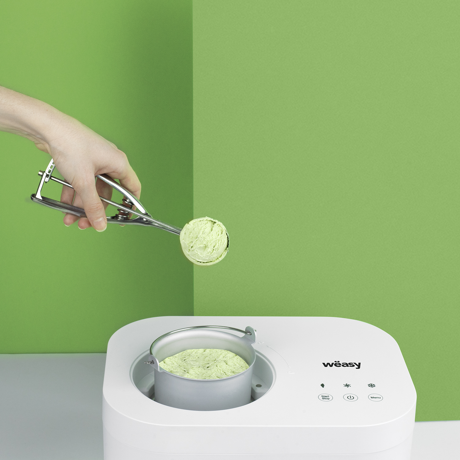 Hand schöpft grünes Eis aus einer weißen Maschine, grüner Hintergrund.