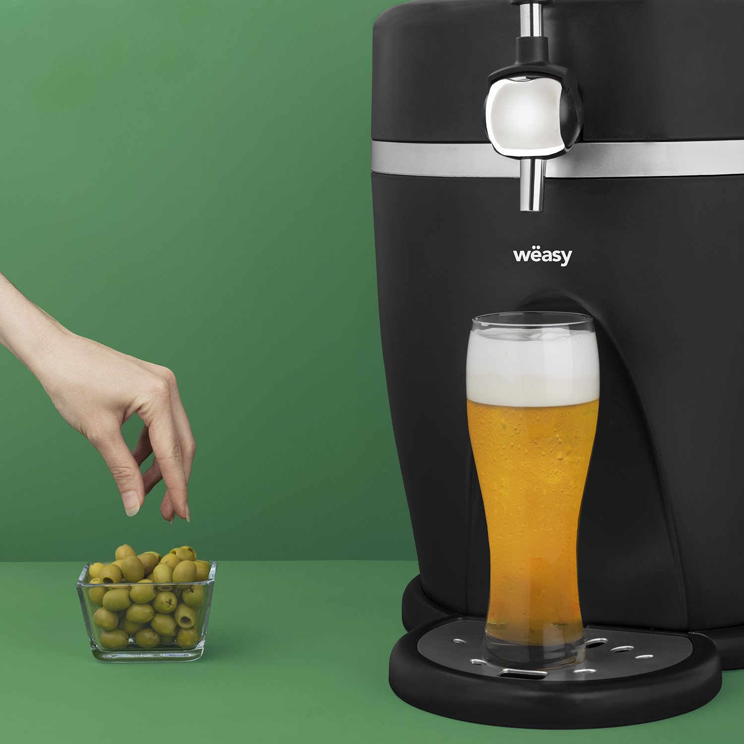 Un grifo de cerveza que dispensa cerveza en un vaso. Aceitunas en un cuenco a la izquierda.