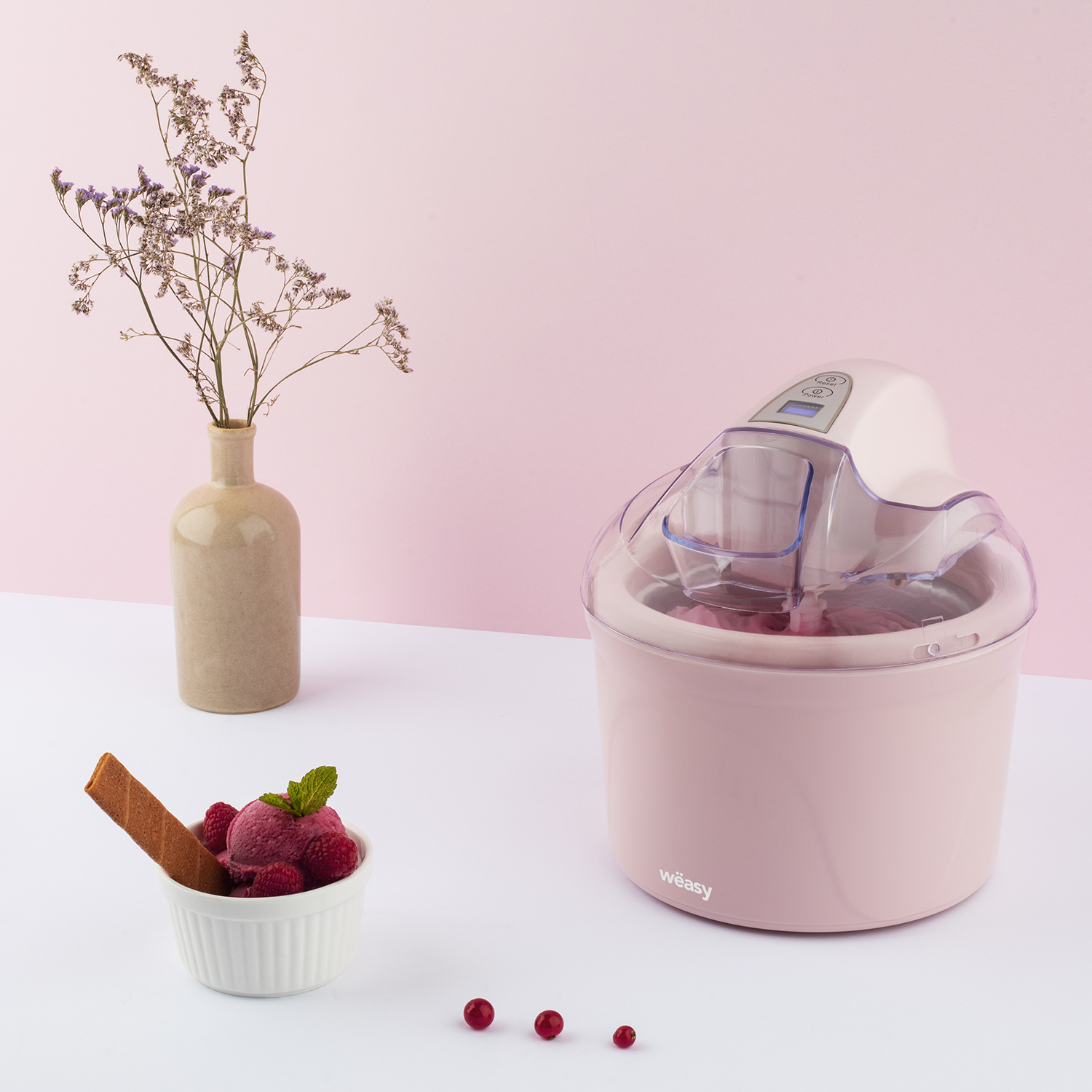 Rosa Eismaschine mit Eis und Deko auf einem weißen Tisch. Der Hintergrund ist rosa.