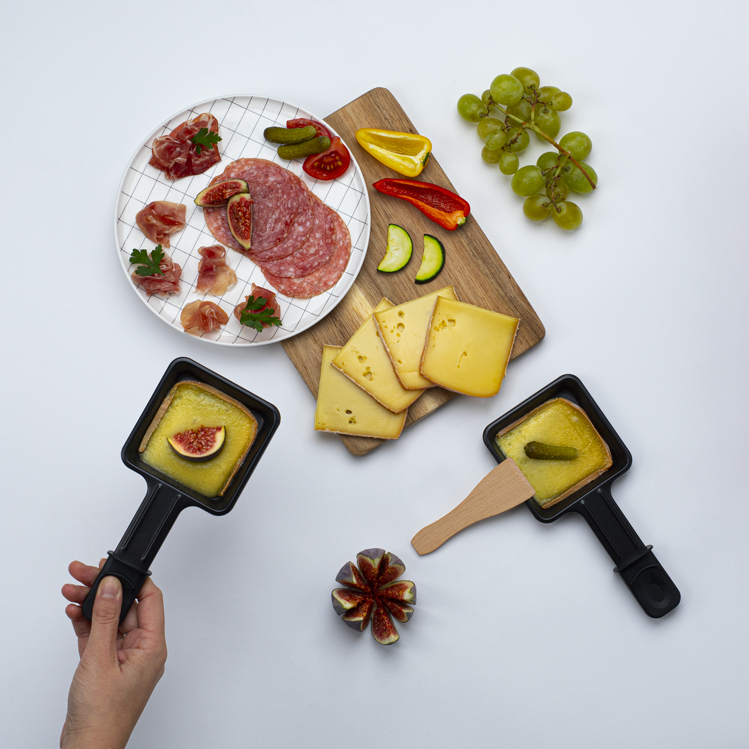 Ein Tisch mit verschiedenen Gourmet-Lebensmitteln: Fleisch, Käse, Obst und Raclette-Pfannen.