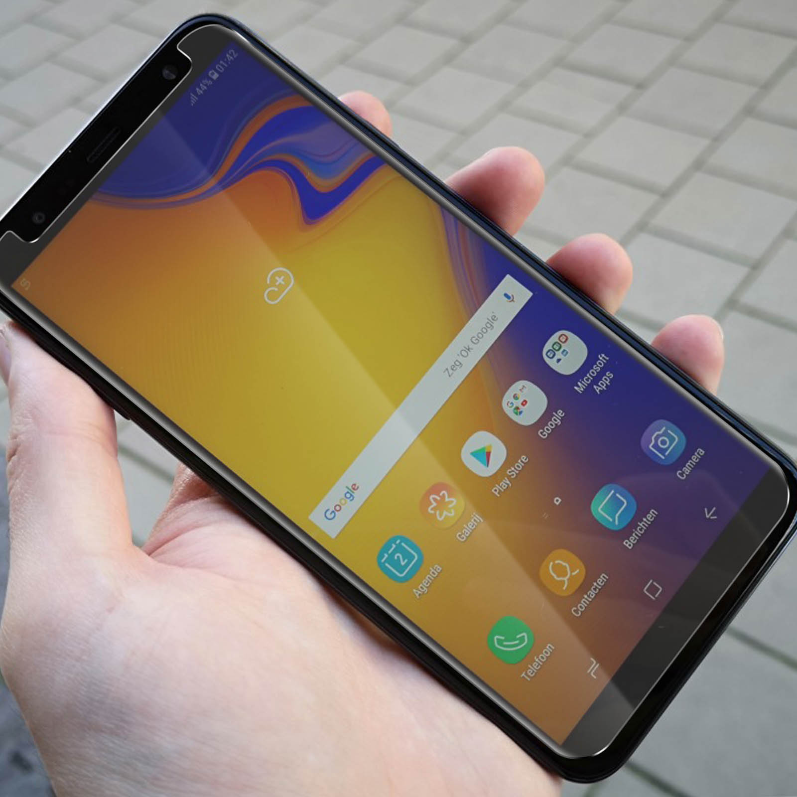 Mano che tiene uno smartphone con protezione schermo applicata. Il telefono mostra la schermata iniziale.