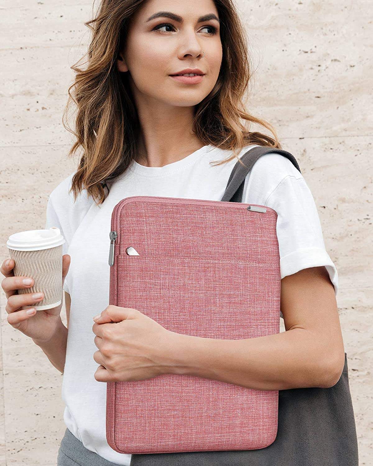 Frau hält eine Laptoptasche und eine Kaffeetasse. Sie trägt ein weißes Hemd und steht in der Nähe eines Gebäudes.