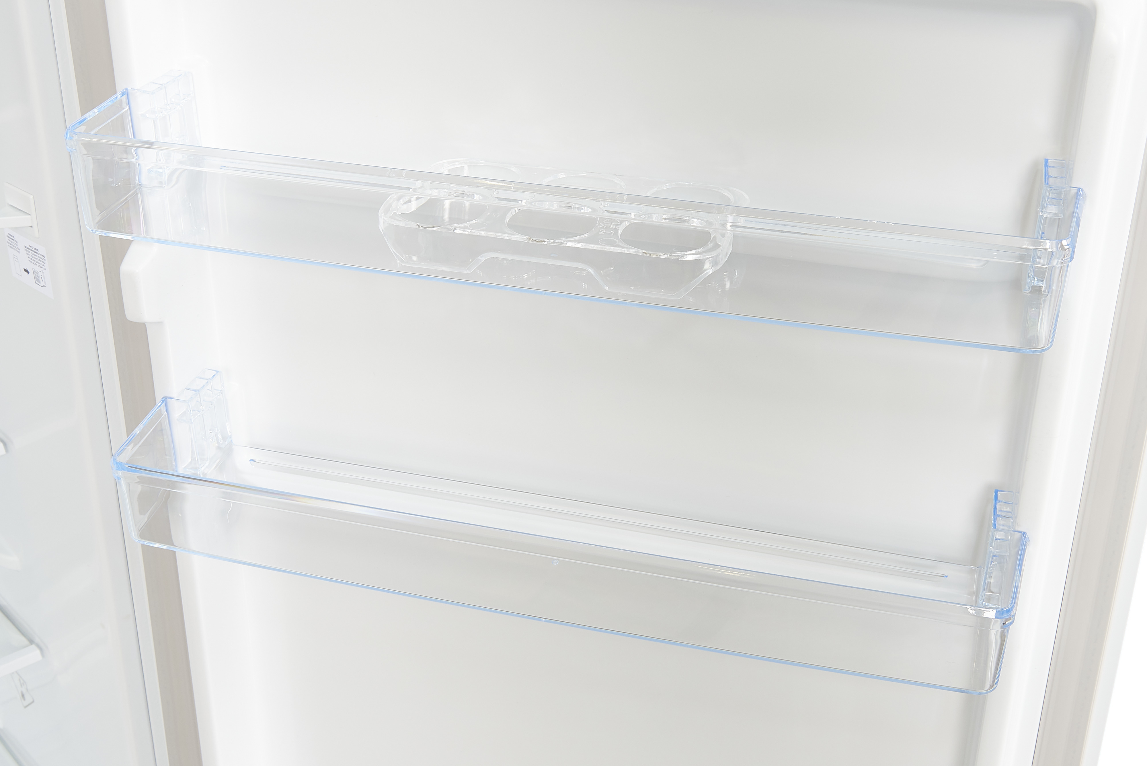 El interior de un refrigerador, mostrando estantes transparentes y un recipiente para botellas.