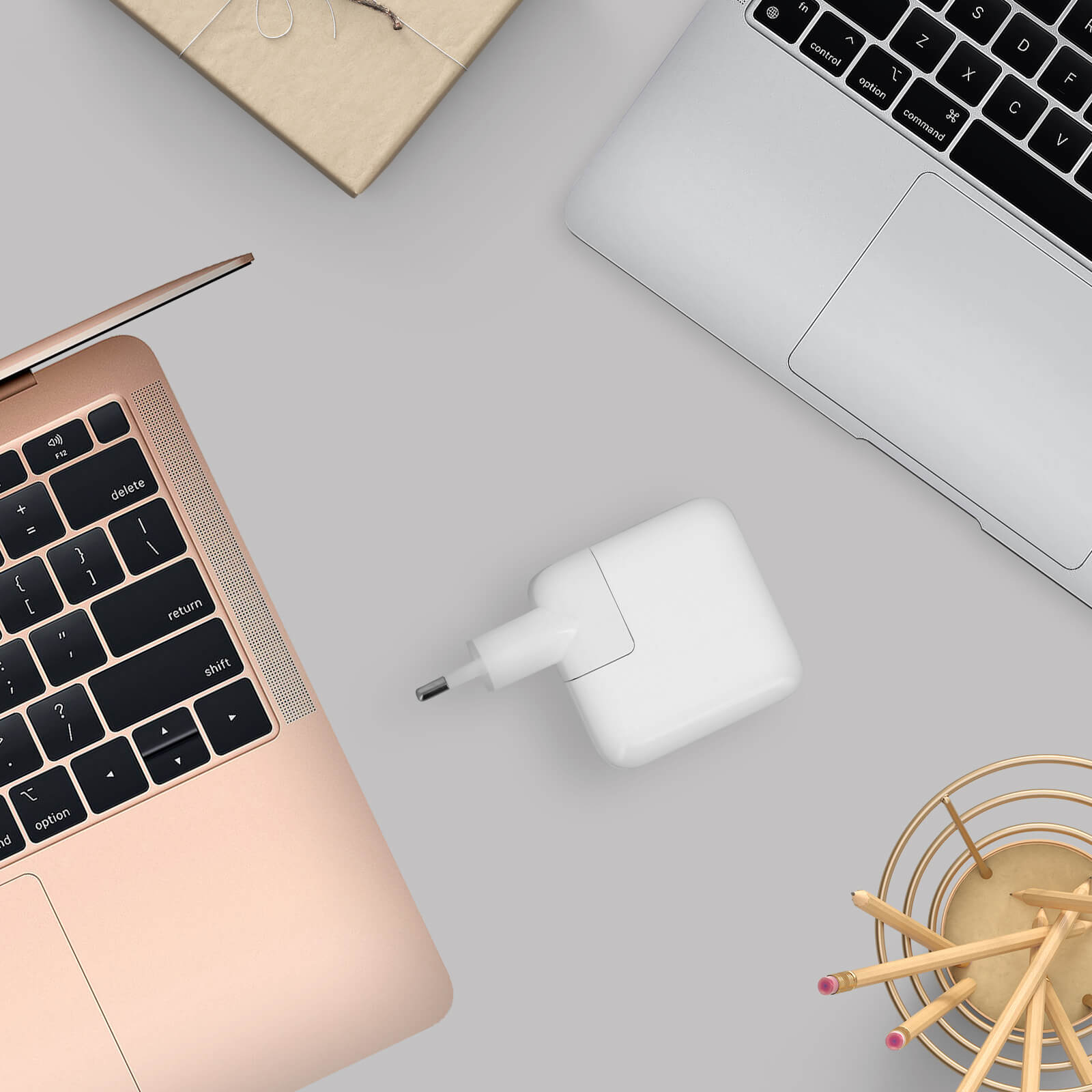 Laptop, caricatore, matite e un pacco regalo su una superficie grigio chiaro.