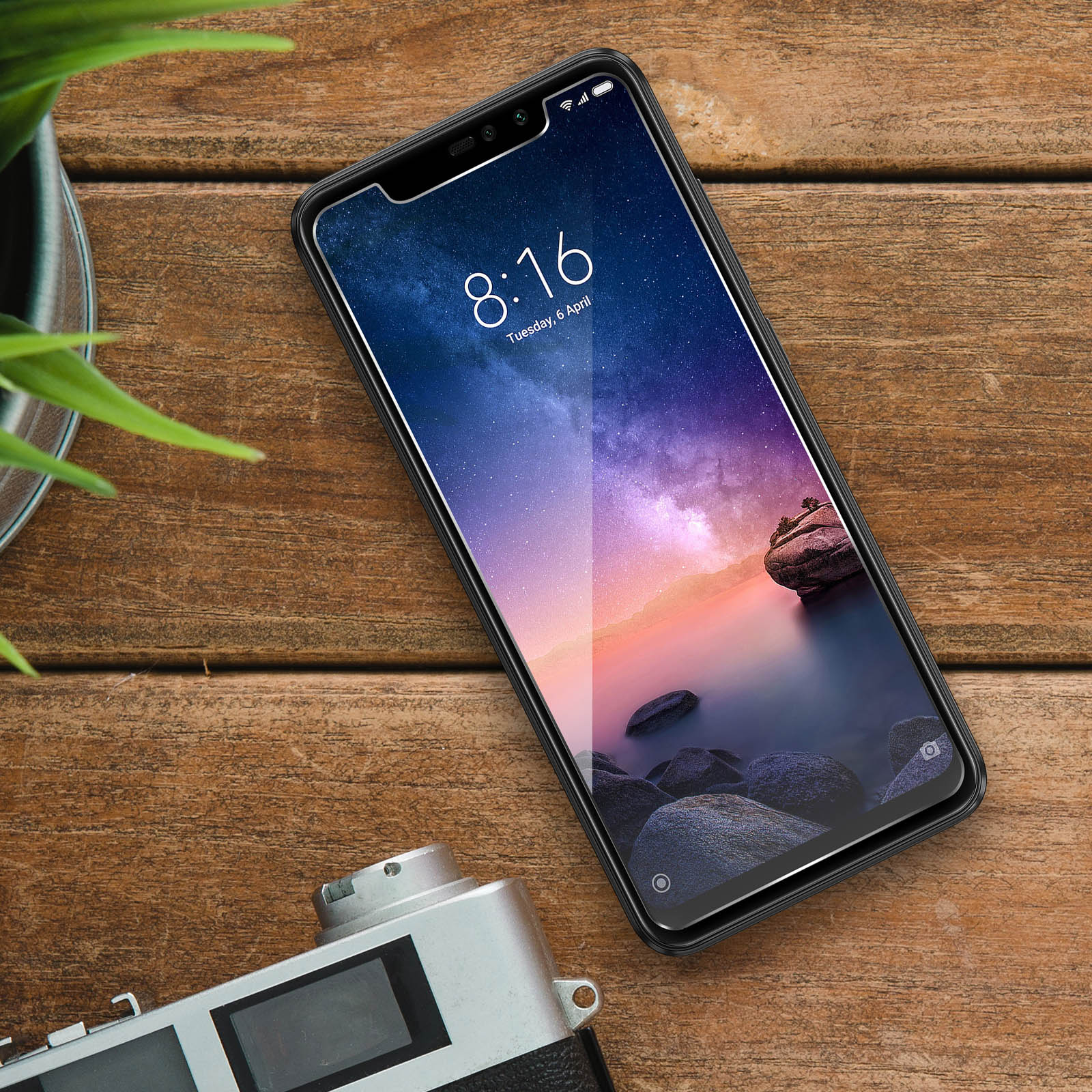 Uno smartphone con una protezione per lo schermo su un tavolo di legno, che mostra un'immagine del paesaggio. C'è una fotocamera accanto.