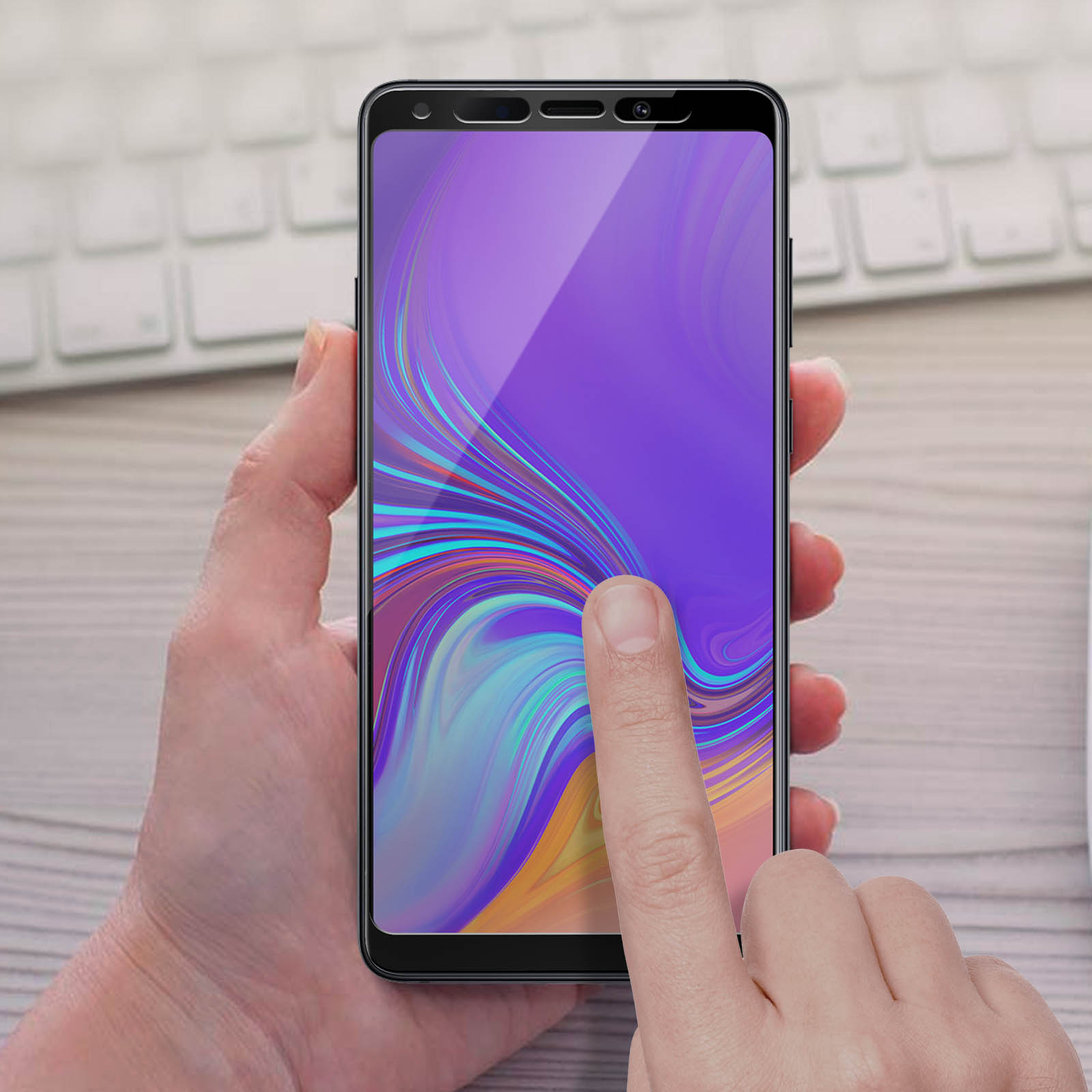 Mano che tiene un telefono che mostra una grafica colorata. Dito che tocca lo schermo. Tastiera visibile sullo sfondo.