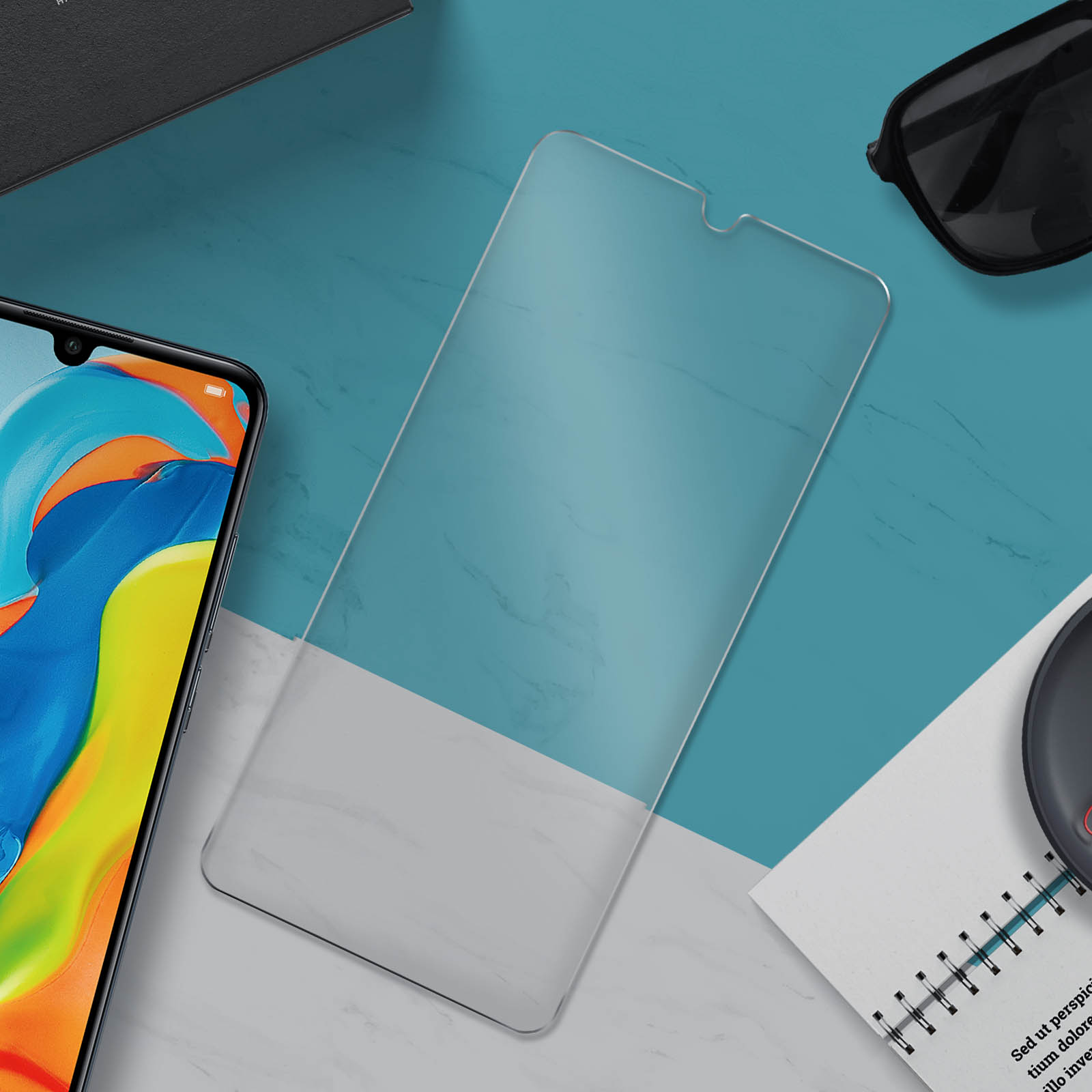 Una protezione schermo trasparente e un telefono. Una superficie blu e bianca con occhiali da sole e blocco note.