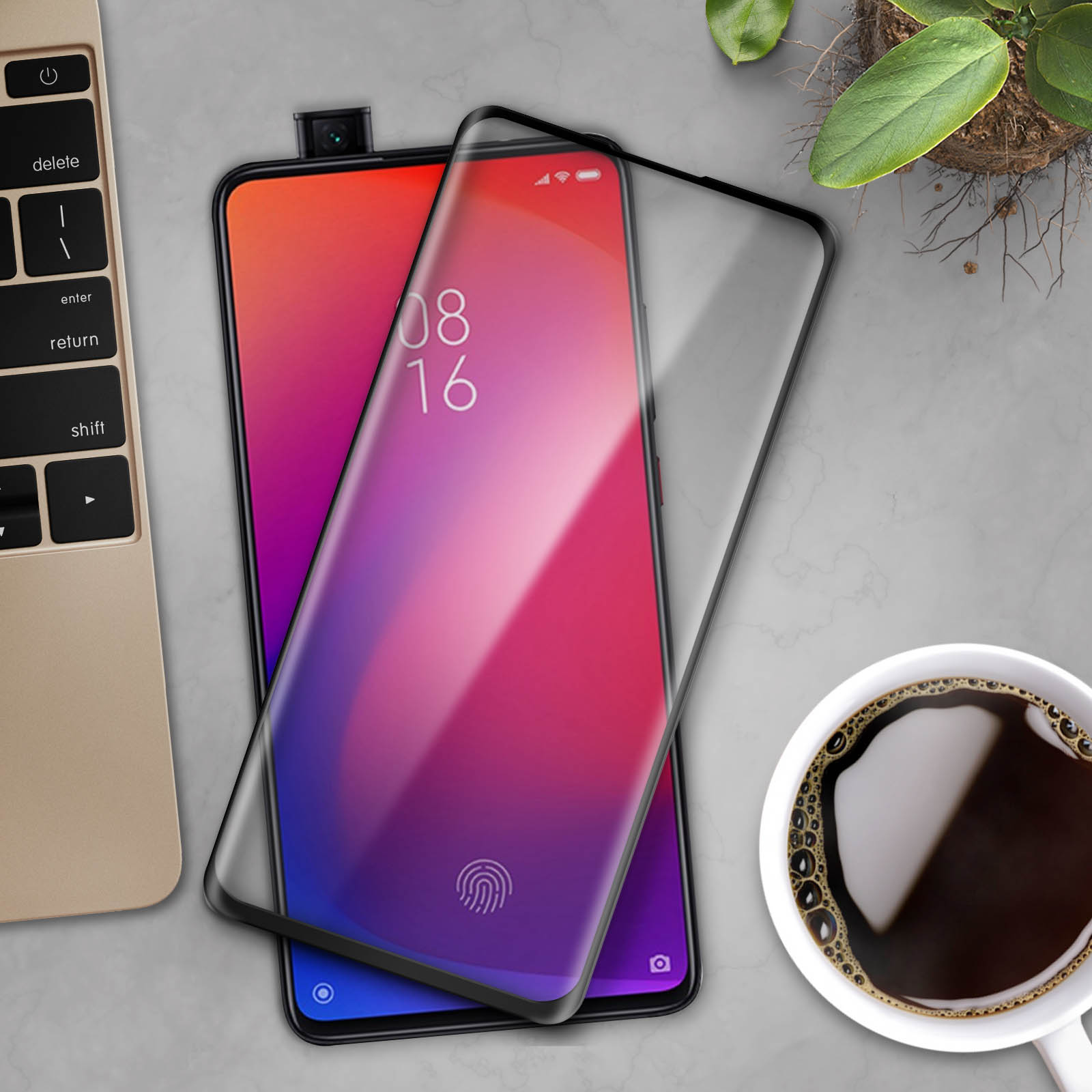 Telefono con protezione schermo. Laptop, tazza di caffè e pianta sullo sfondo.