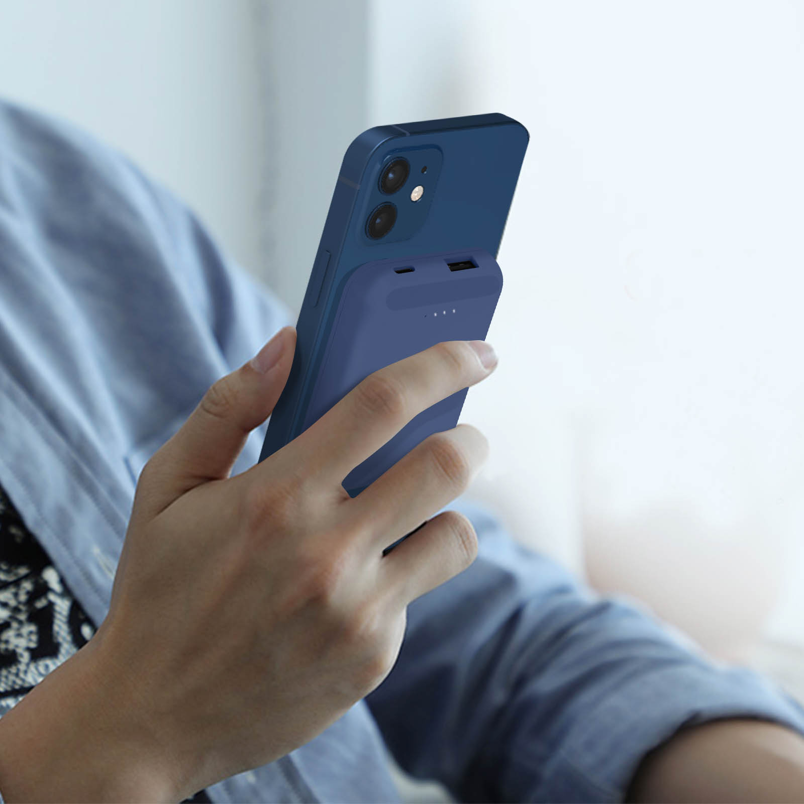 Die Hand einer Person, die ein Telefon mit einer blauen Powerbank hält. Der Hintergrund ist unscharf.