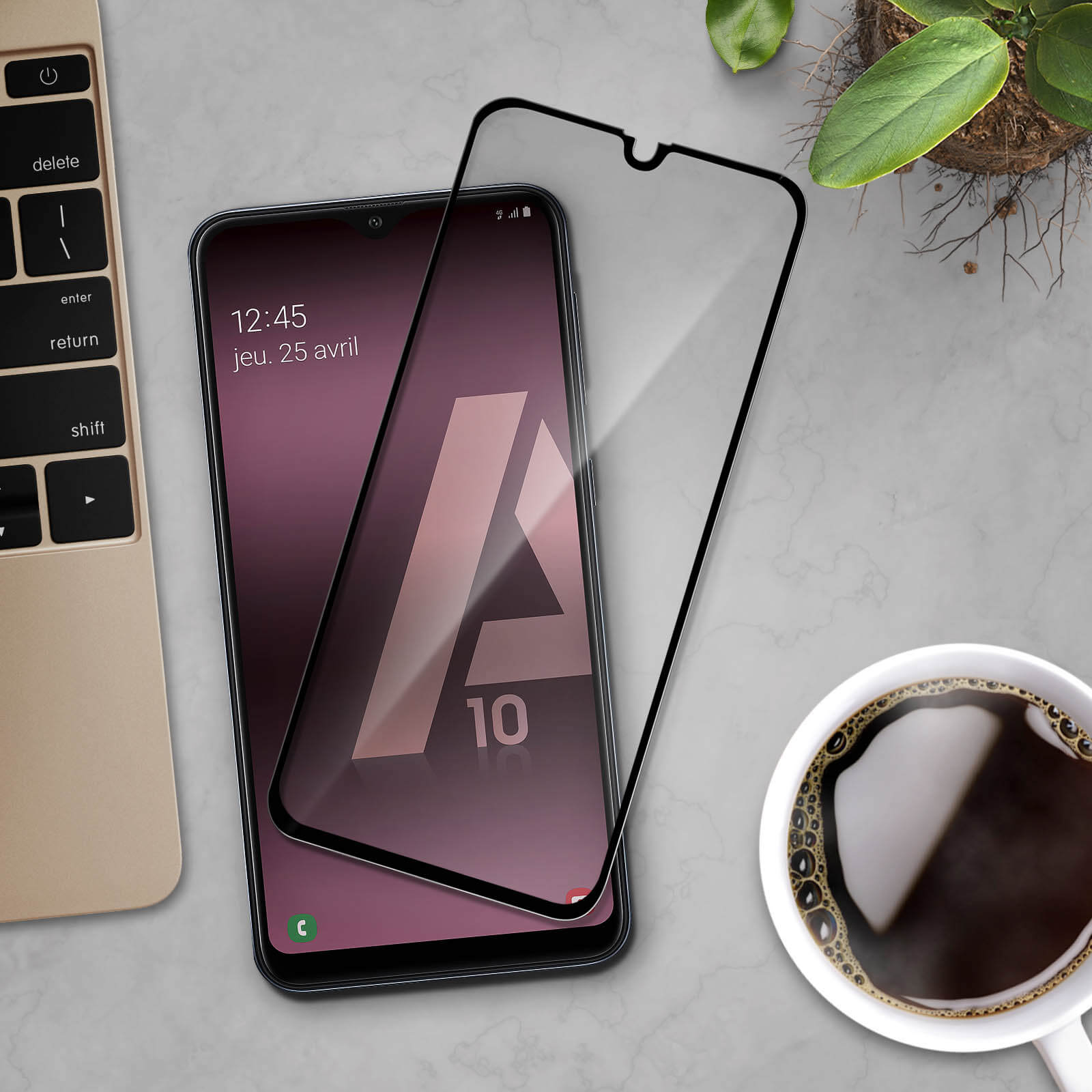 Telefono e protezione schermo. Lo schermo mostra ora e data. Laptop, caffè e pianta.