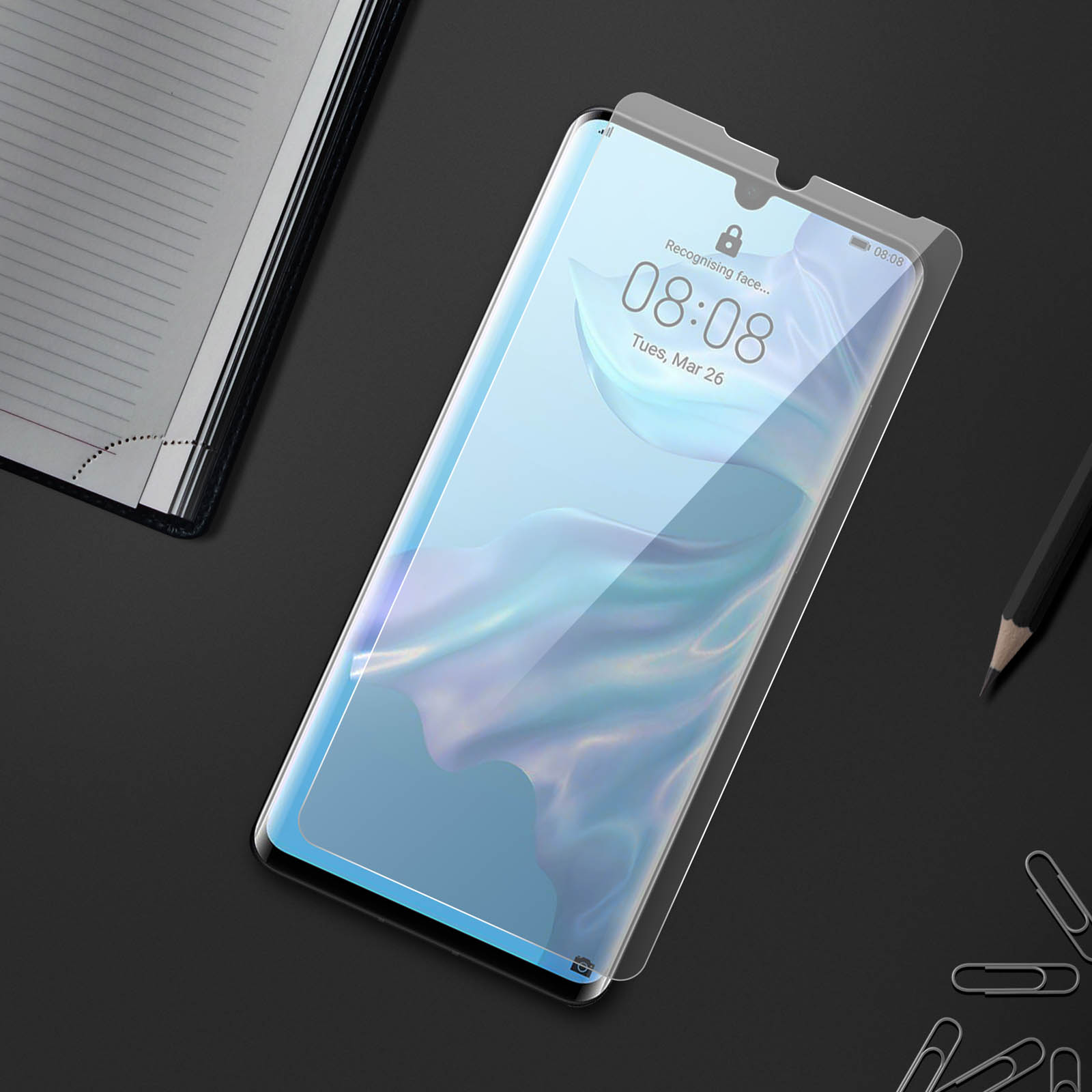 Telefono con protezione schermo su una scrivania. Taccuino e matita sullo sfondo.